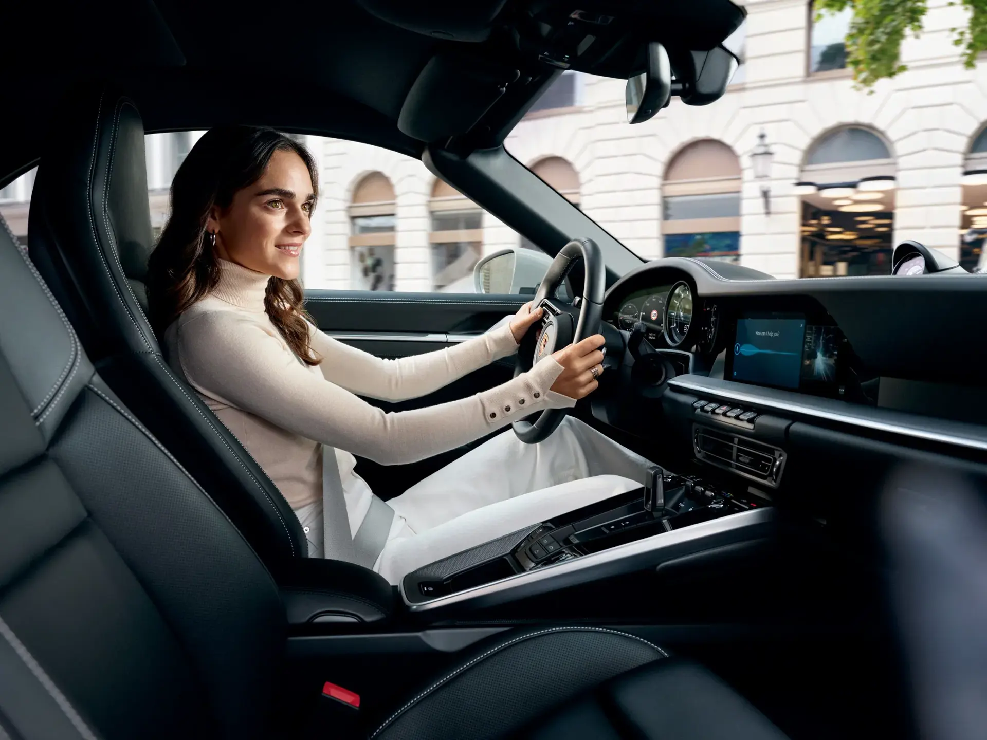 Kvinde sidder smilende bag rattet i en moderne Porsche med digital infotainmentskærm.