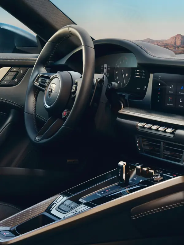 Luksuriøst interiør i en Porsche 911 Turbo S med rat, digital instrumentering og midterkonsol set fra førersædet.