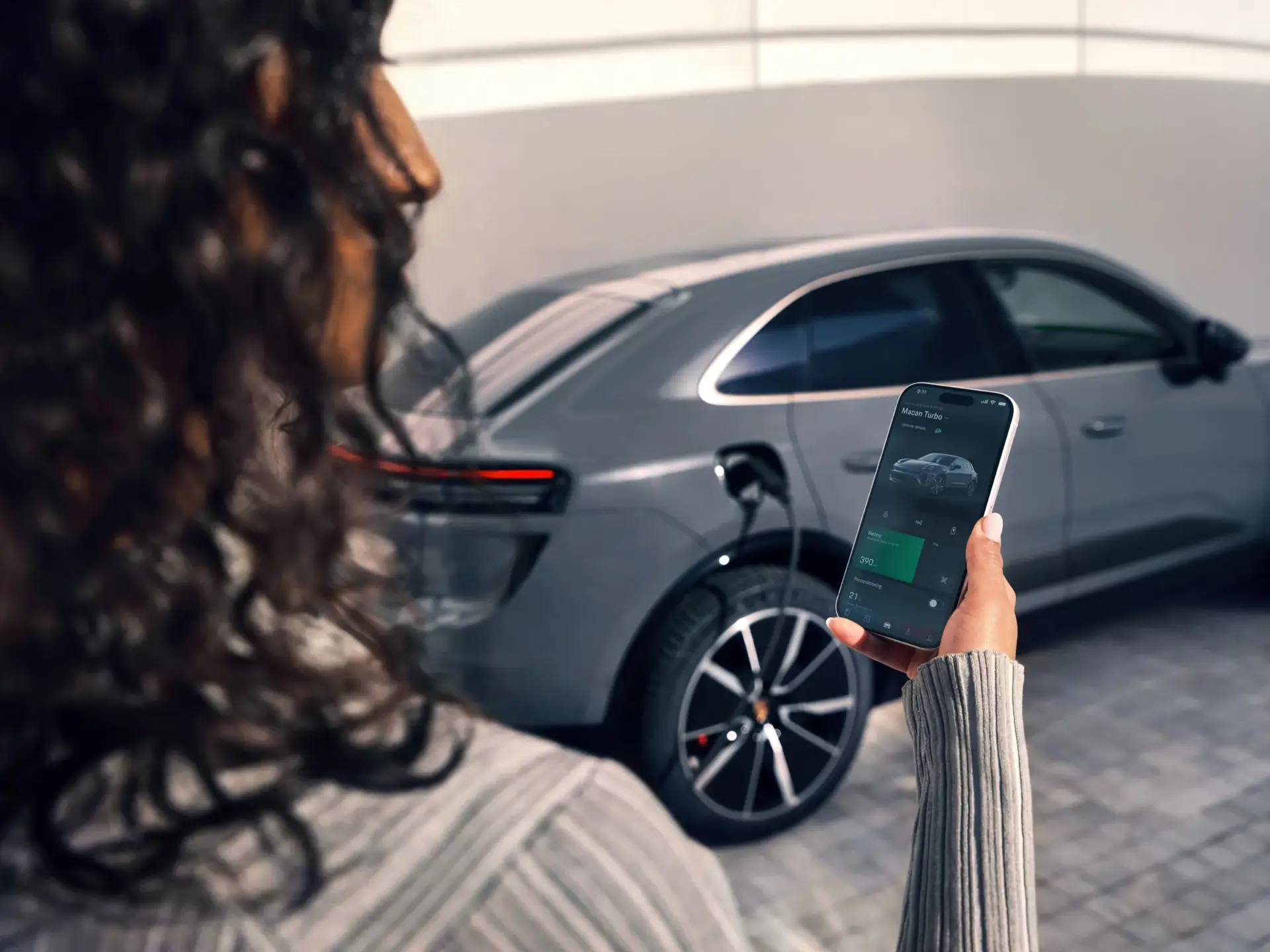 Person styrer opladningen af en grå Porsche elbil via en My Porsche app på sin smartphone.