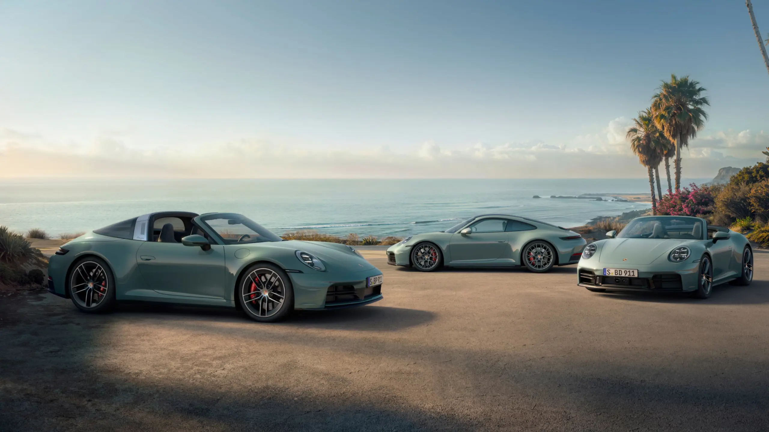 En lysegrå Porsche 911 Carrera 4S cabriolet holder parkeret ved en moderne kystvilla med udsigt over havet i solnedgangen.