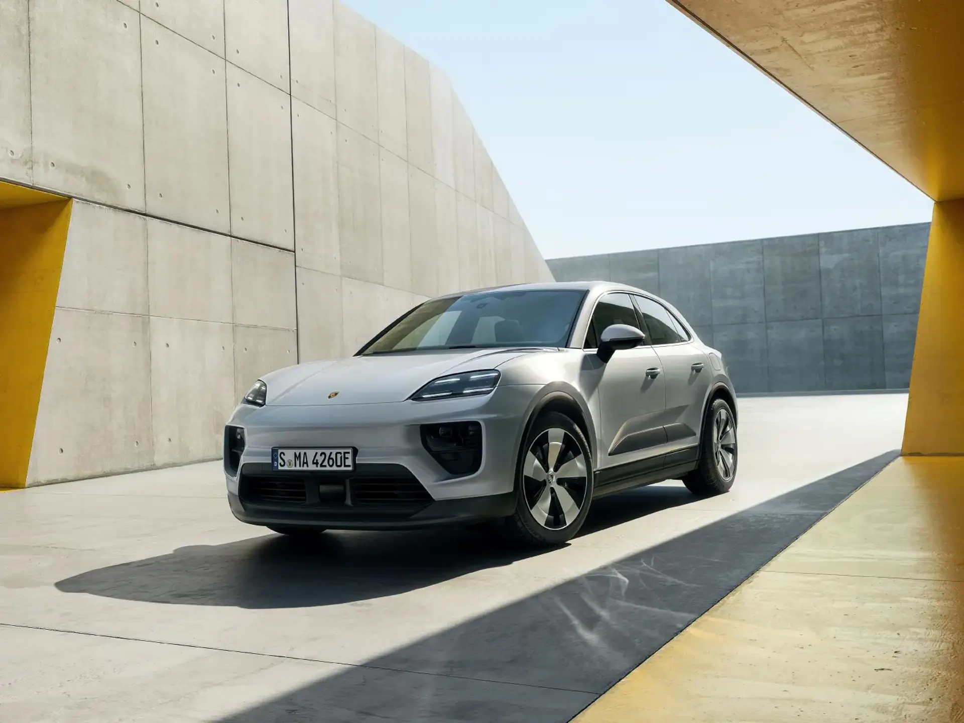 Sølvgrå Porsche Macan står parkeret i et moderne, minimalistisk betonmiljø med gule detaljer.