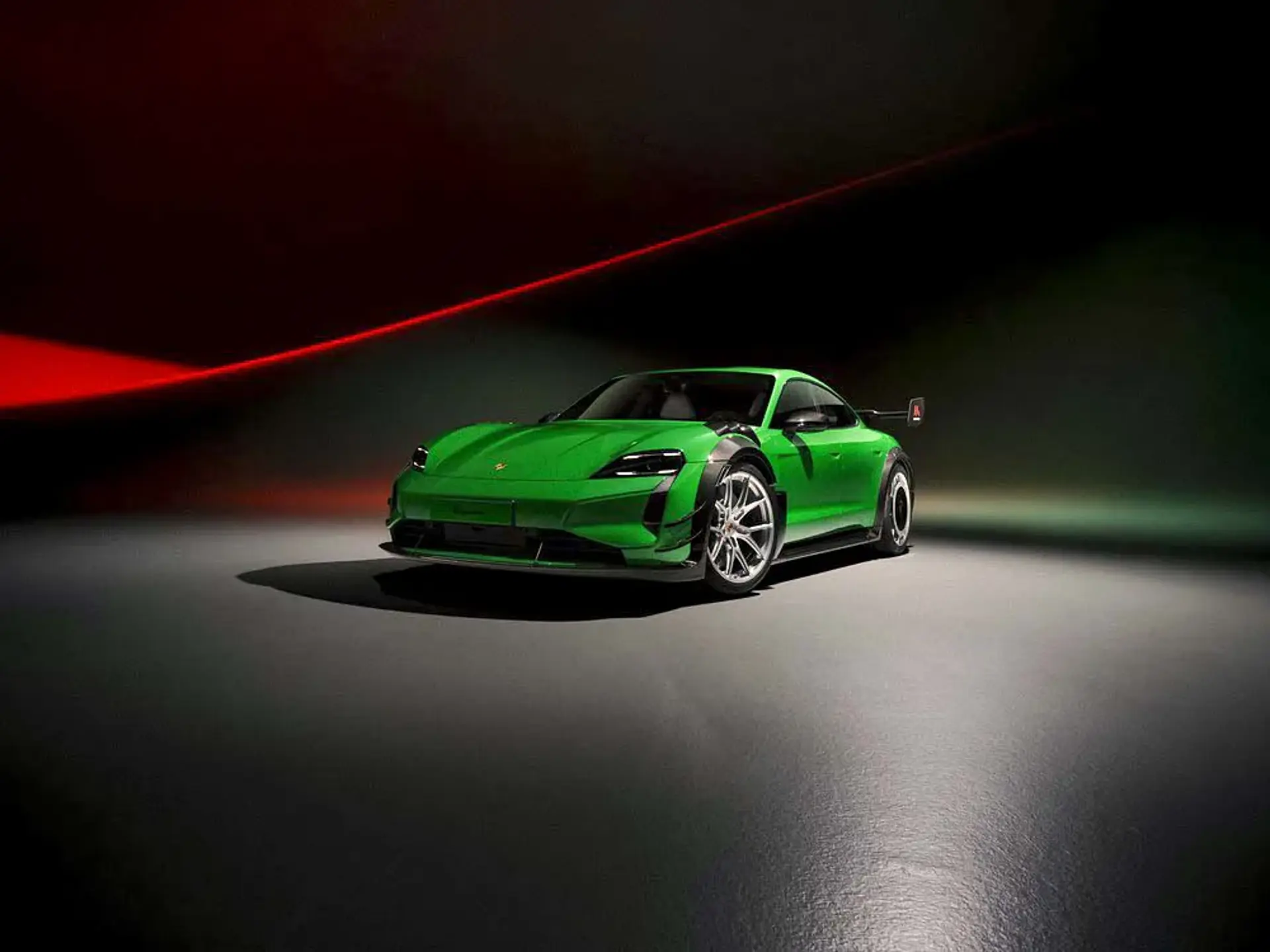 Grøn Porsche Taycan Manthey vises i en mørk studieopstilling med dramatisk rød og grøn belysning.
