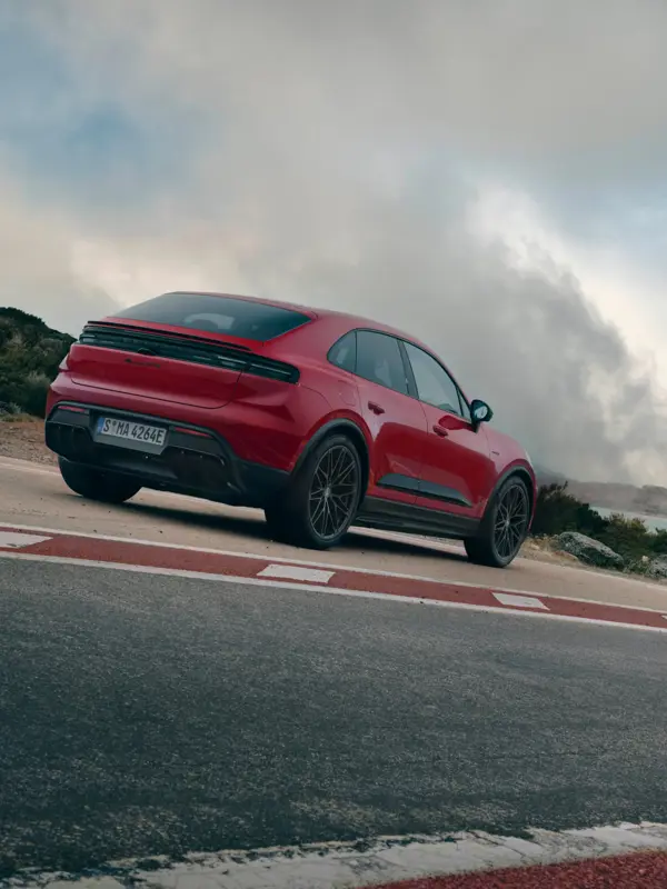 Rød Porsche Macan GTS set bagfra parkeret på en landevej med dramatiske skyer i baggrunden.