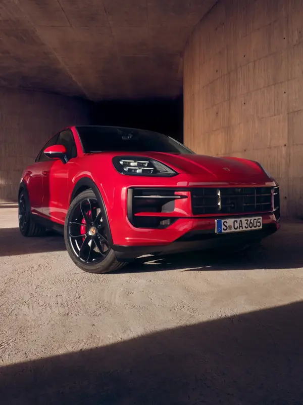 Rød Porsche Cayenne GTS Coupé holder parkeret i et råt betonmiljø med skygger på jorden.