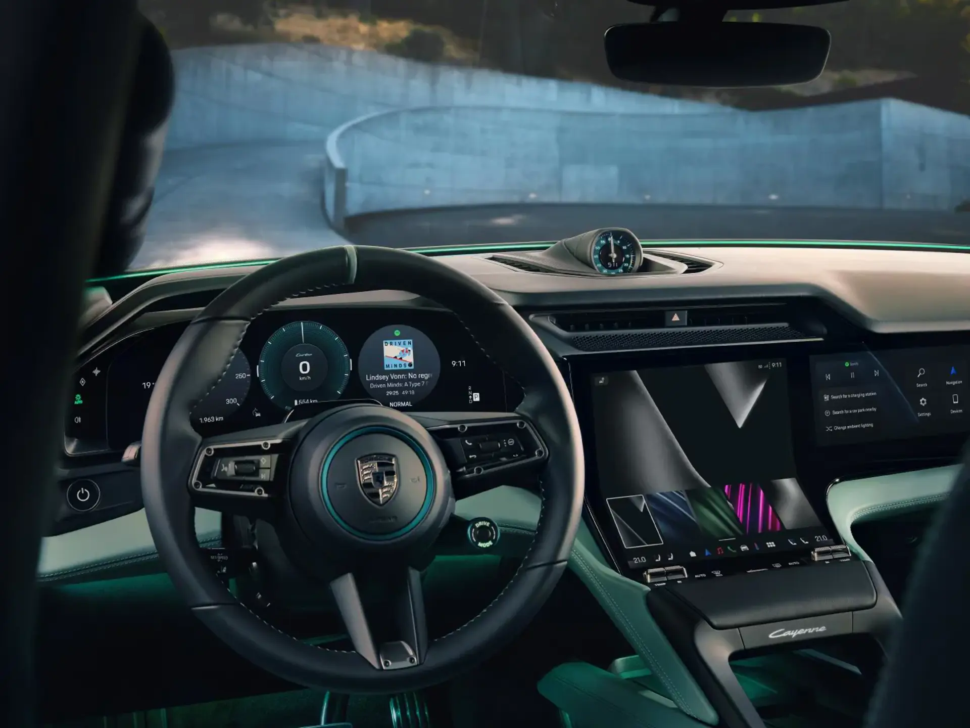 Førerpladsen i en elektrisk Porsche Cayenne med digitalt cockpit, stor midtertouchskærm og udsigt gennem forruden til en vej.