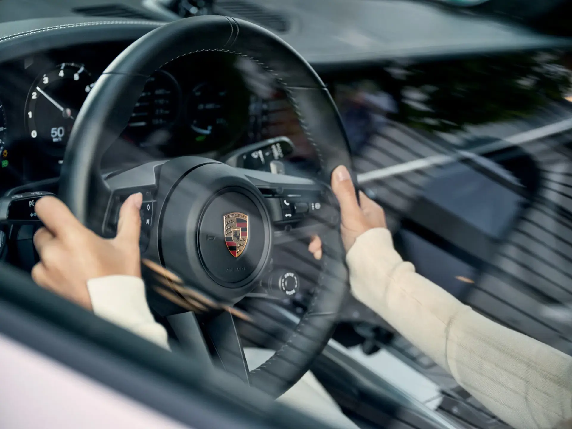Person der holder om rattet i en Porsche med fokus på instrumentbrættet og logoet.