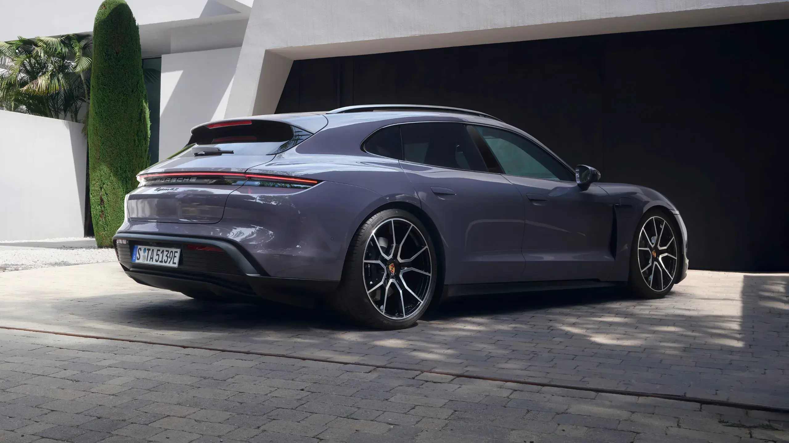 En grå Porsche Taycan 4S Sport Turismo kører hurtigt på en åben vej under blå himmel.