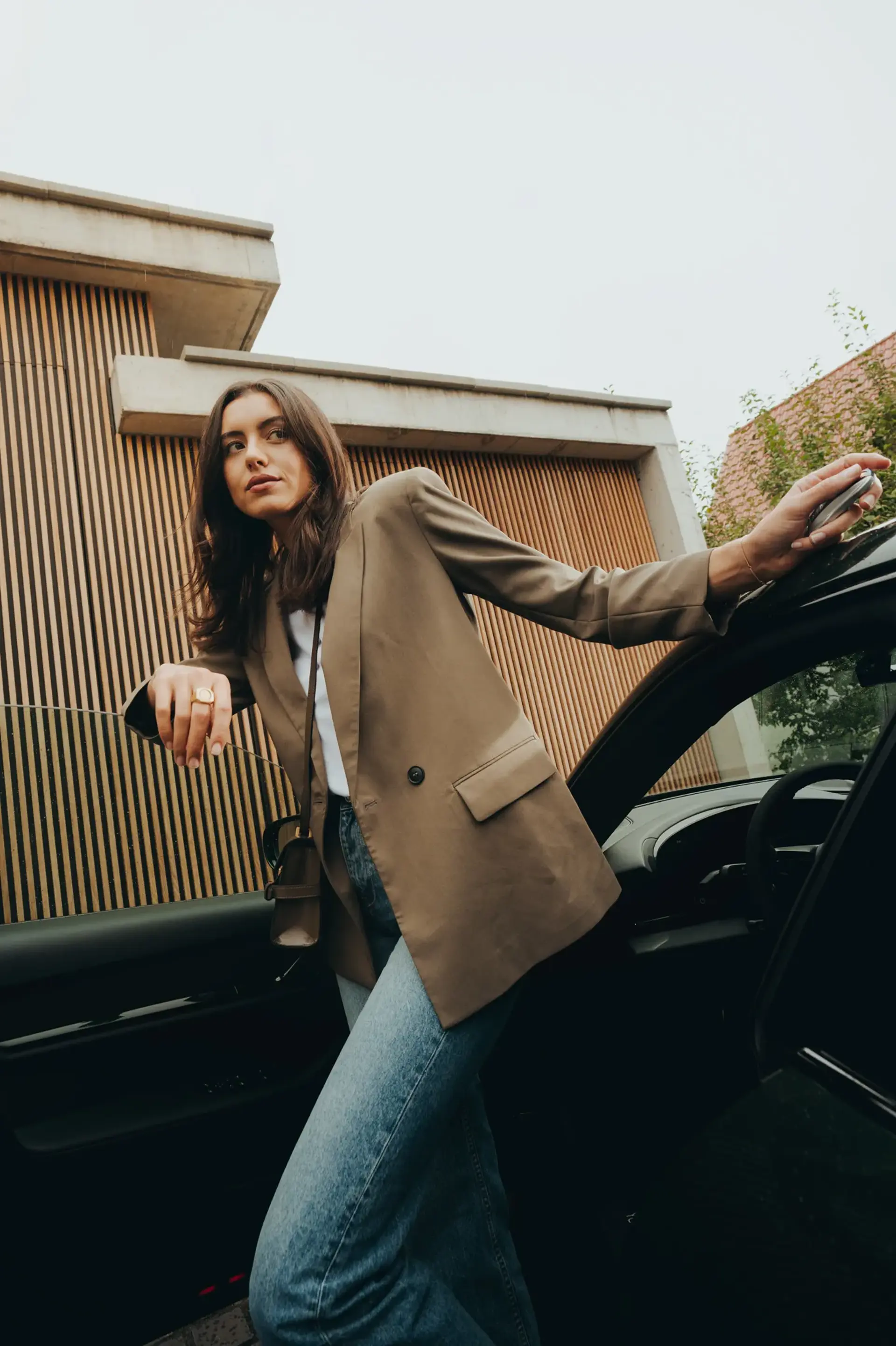 Kvinde i blazer og jeans stiger ud af en sort bil foran en moderne bygning.