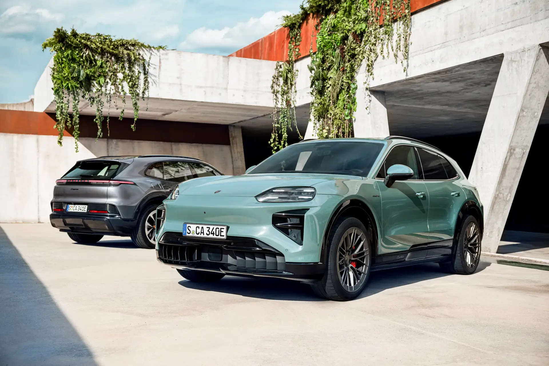 To moderne el-SUV’er holder parkeret foran en betonbygning med hængende grøn beplantning.