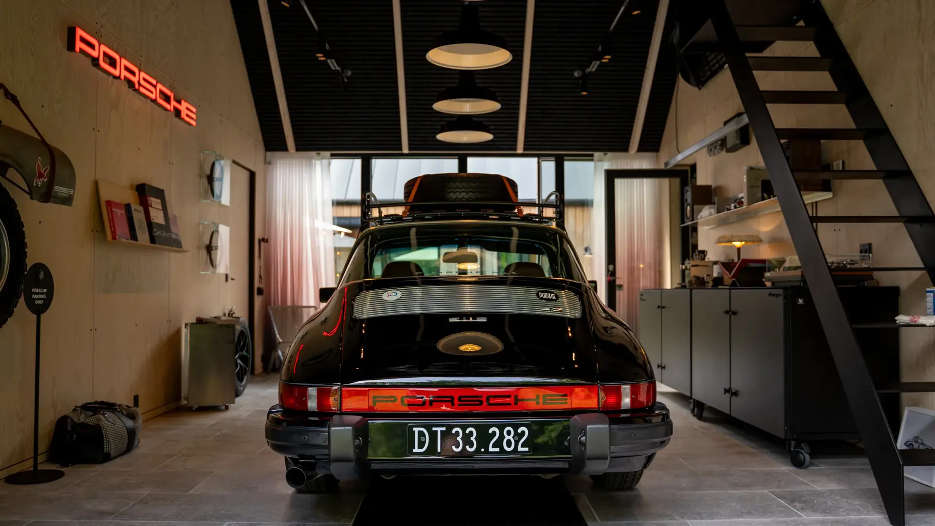 Sort klassisk Porsche sportsvogn set bagfra, parkeret indendørs i et stilfuldt garage- eller værkstedsmiljø.