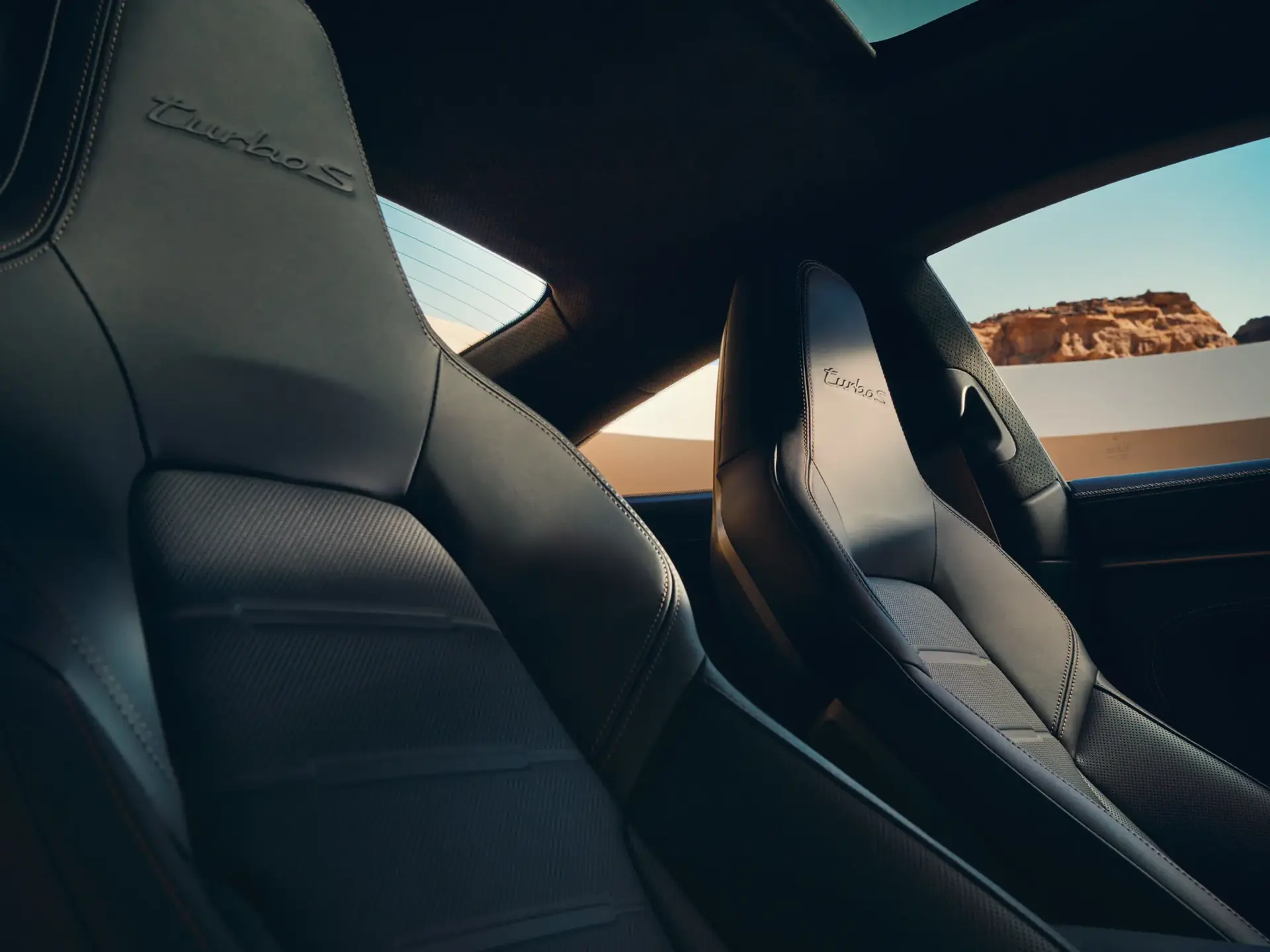 Læderbetrukne sportsforsæder i en Porsche 911 Turbo S med udsigt gennem sideruden til klippelandskab udenfor.