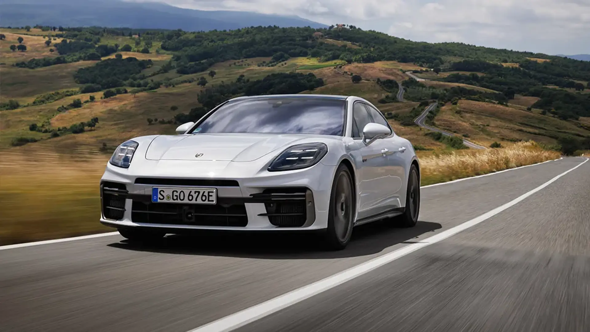 En hvid Porsche Panamera kører på en landevej gennem et kuperet, grønt landskab.