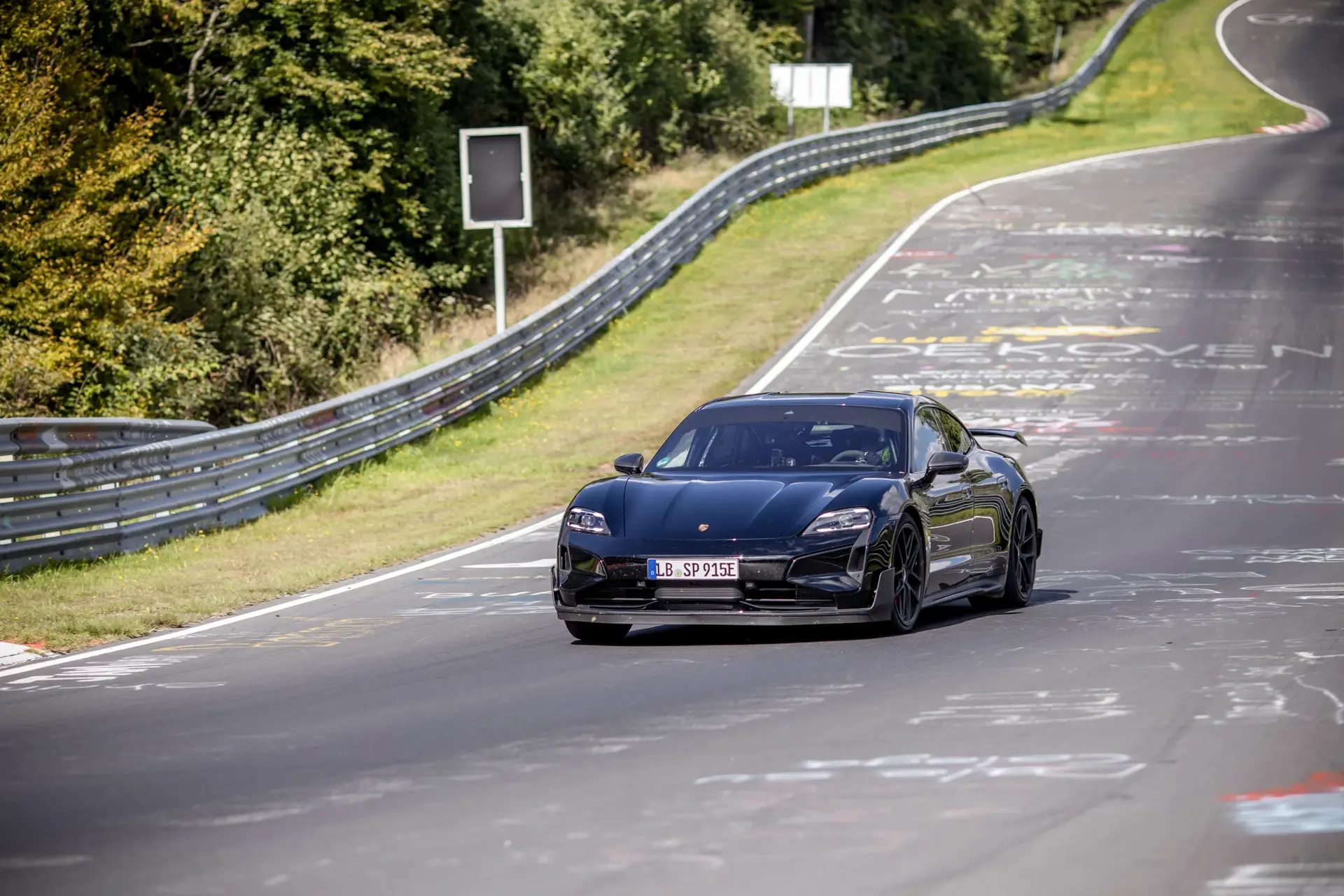 Sort Porsche Taycan i fart på Nürburgring-banen omgivet af skov og autoværn.