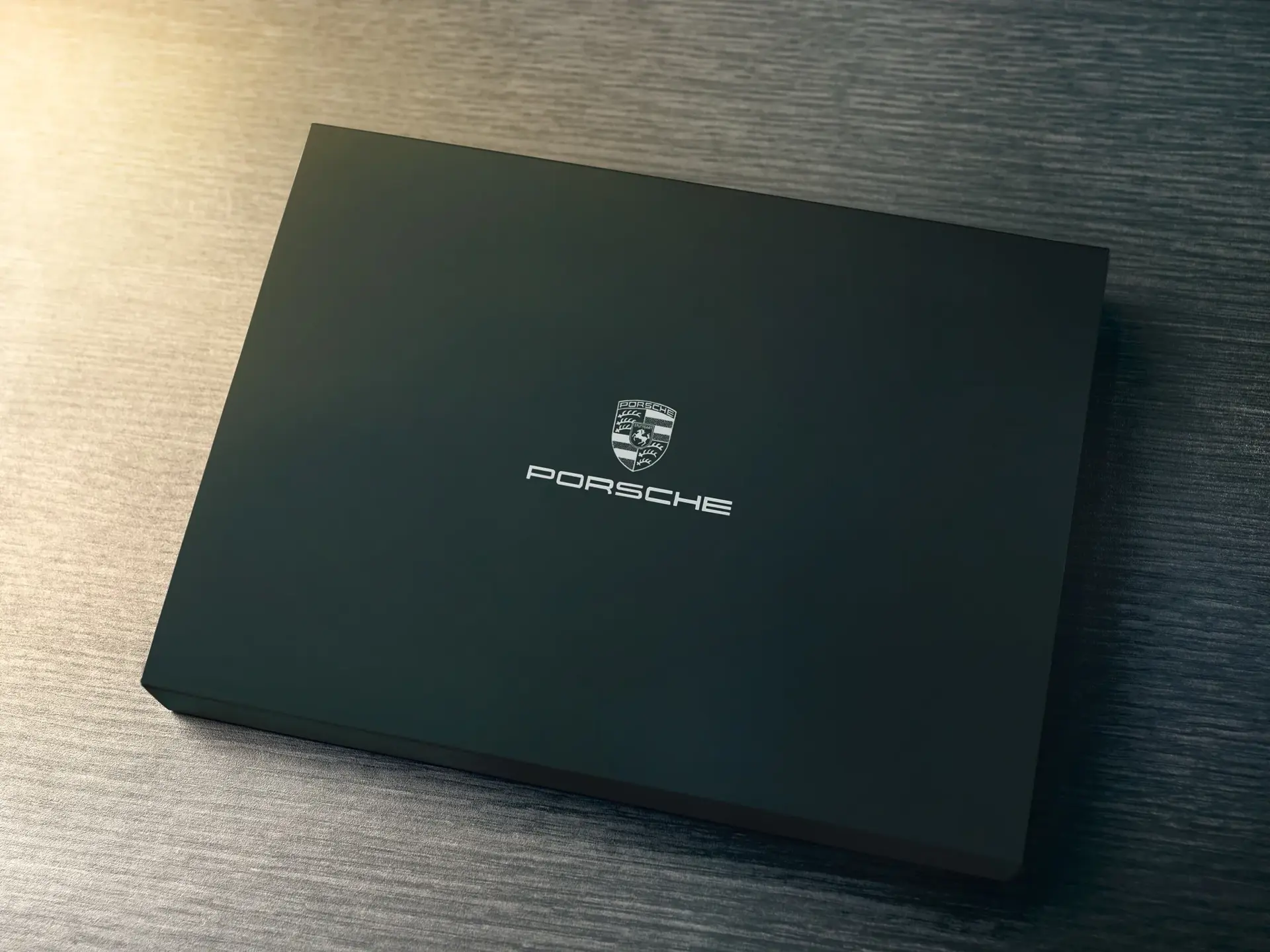 Sort gaveæske med Porsche-logo på låget, set ovenfra på et mørkt bord.