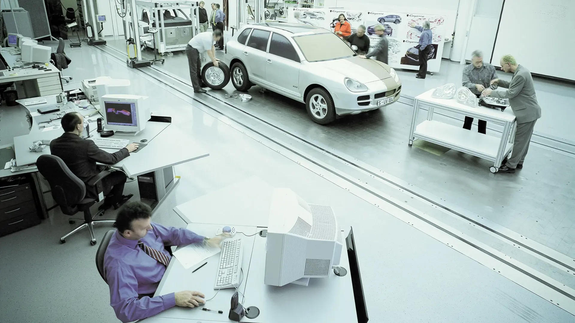 Ingeniører arbejder ved computere og omkring en SUV-prototype i et lyst udviklingsværksted.