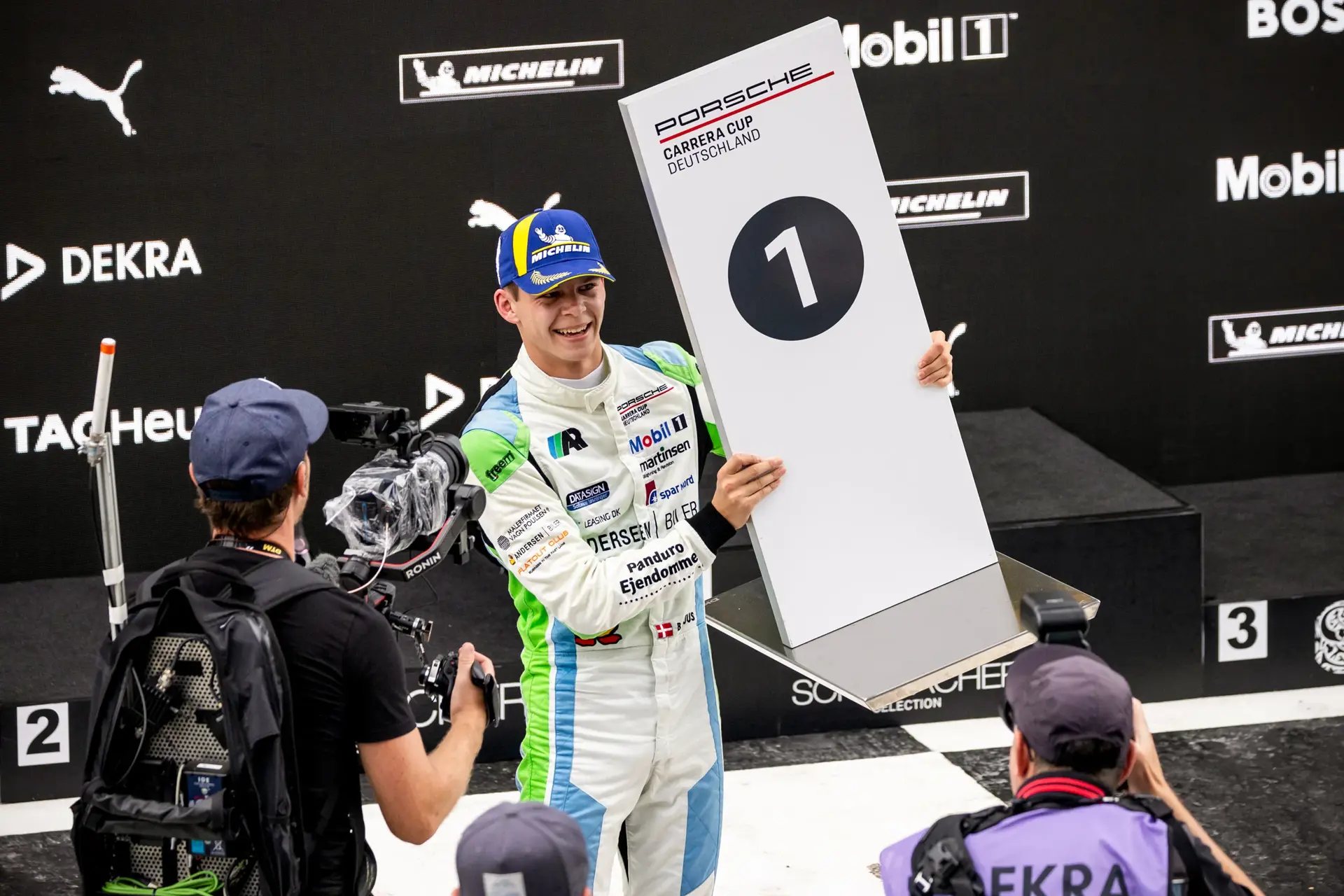 Racerkører på podiet holder et stort skilt med tallet 1 efter en sejr i Porsche Carrera Cup Deutschland.