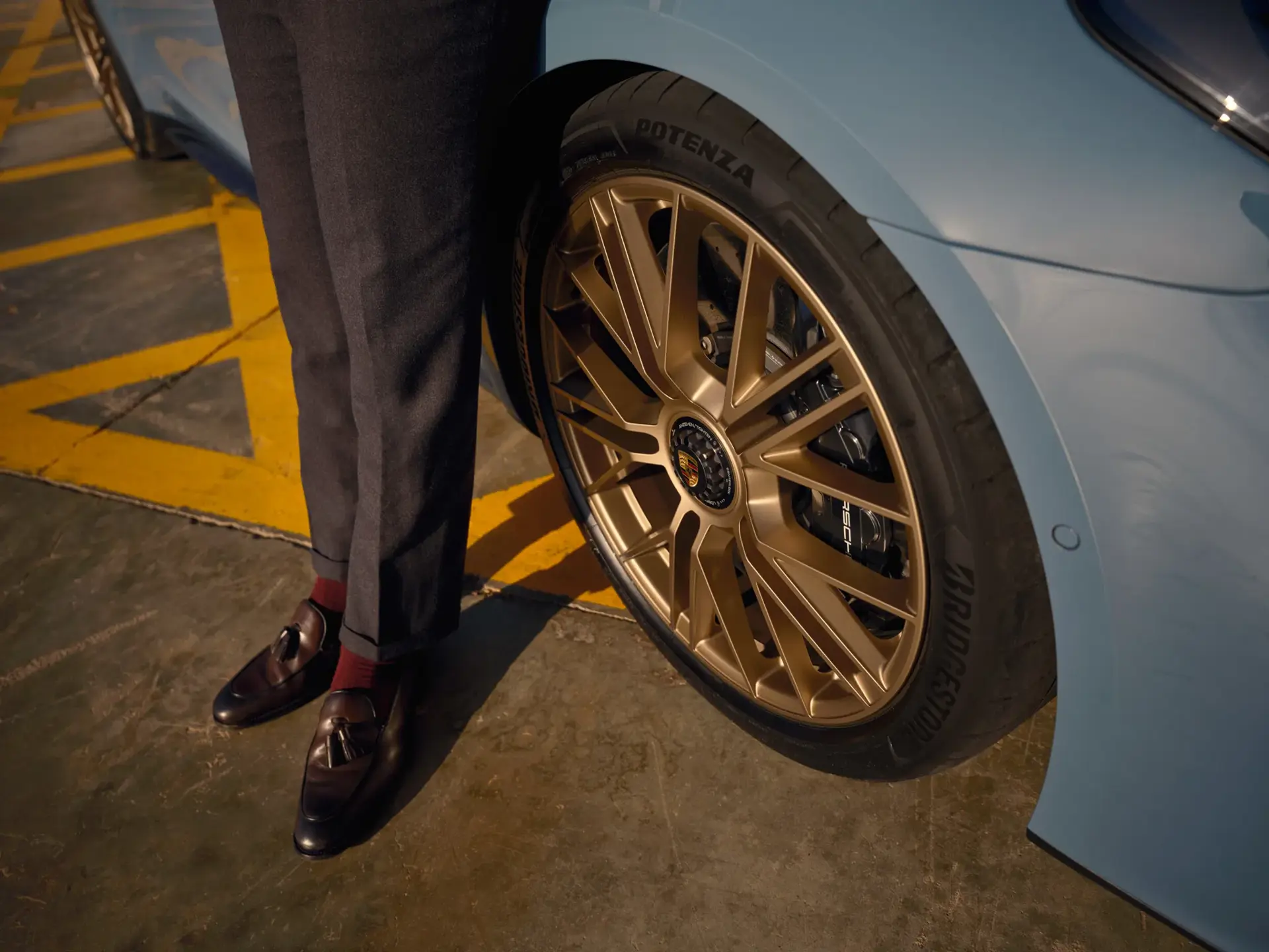 Mand i elegante sko står ved baghjulet på en lyseblå Porsche Panamera med gyldne fælge.