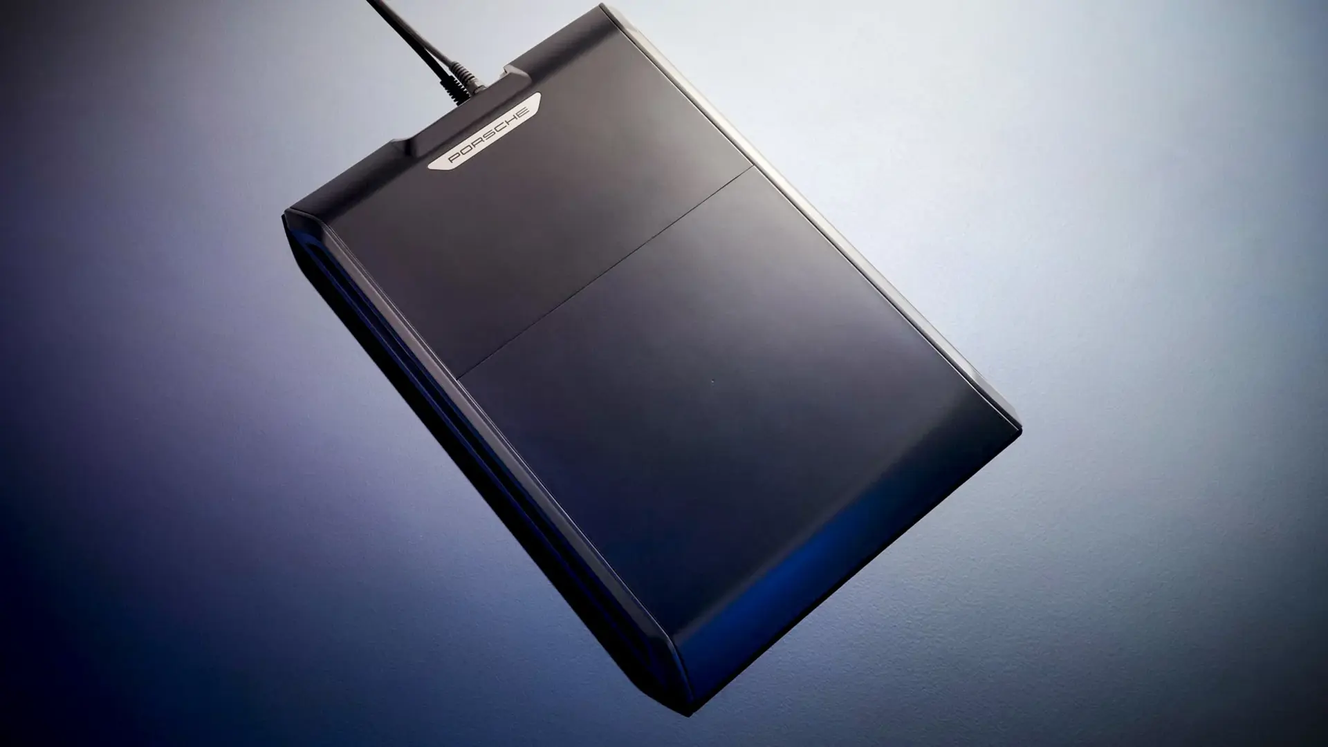Sort ekstern harddisk med Porsche-logo set oppefra mod en blå baggrund.