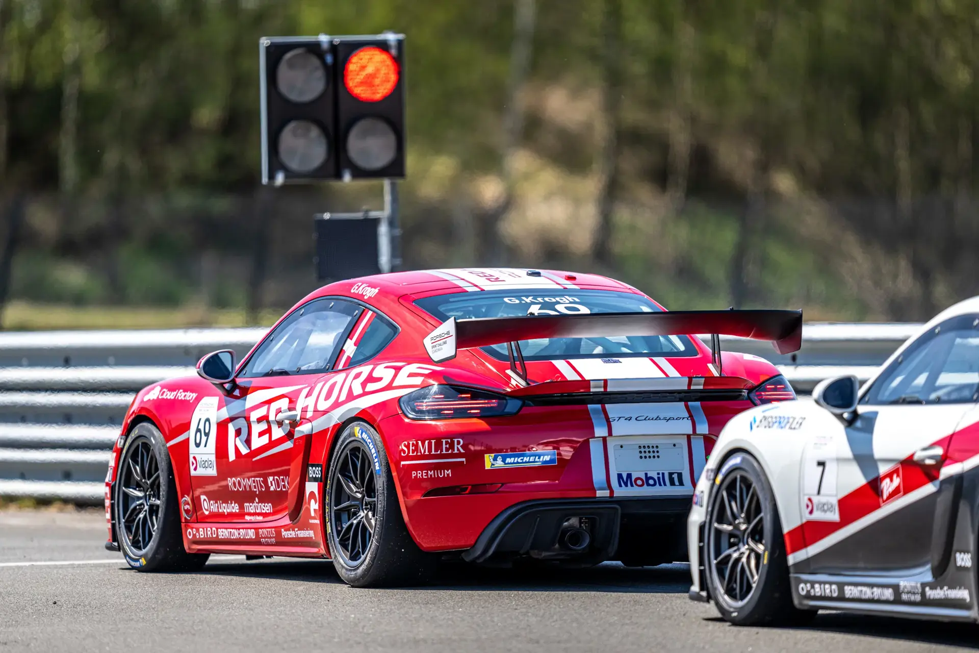 To Porsche-racerbiler holder stille ved rødt lys på racerbane under et løb.