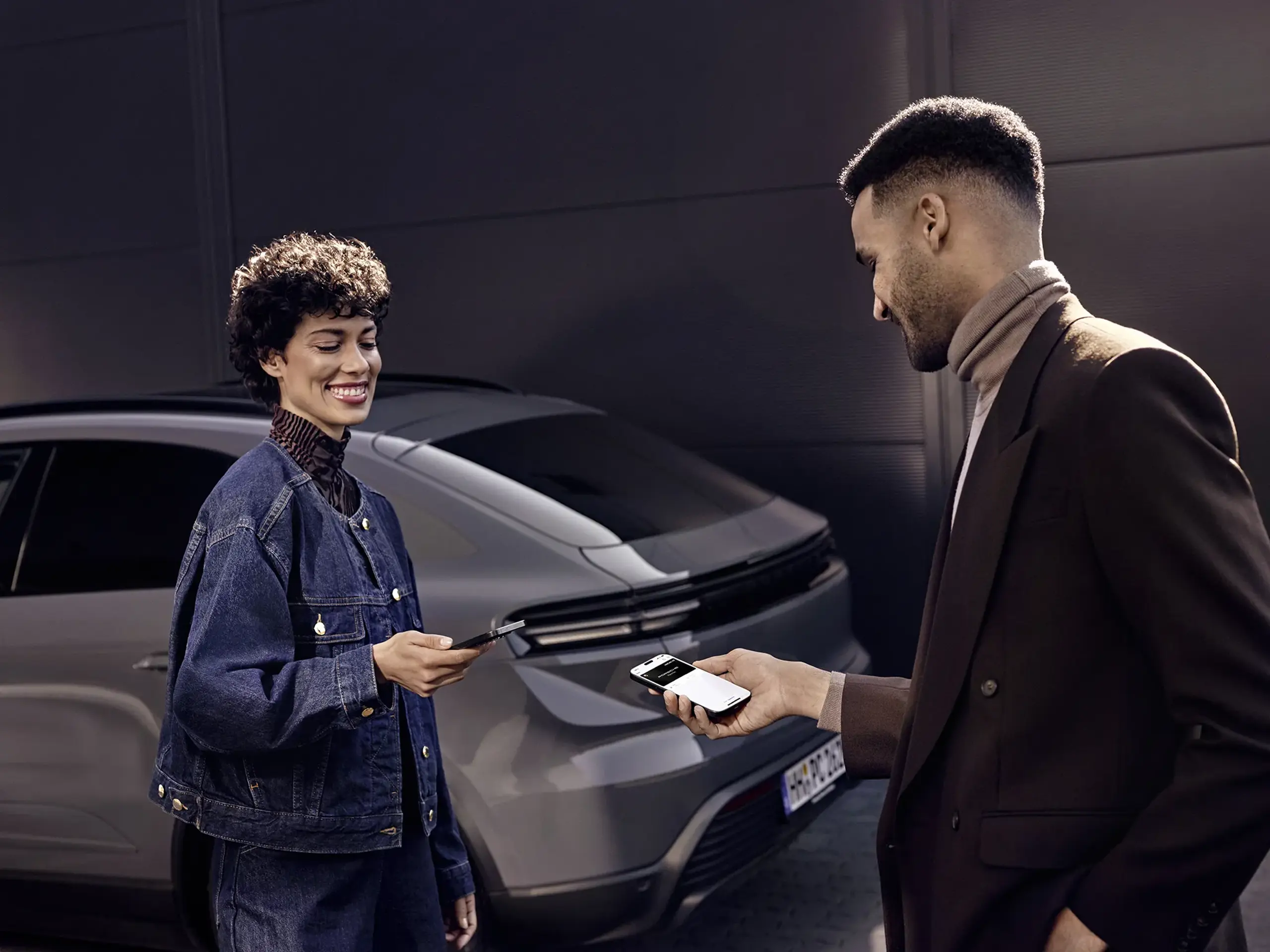 Smilende person foran en bil holder en smartphone op med Porsche Connect digital nøgle på skærmen.