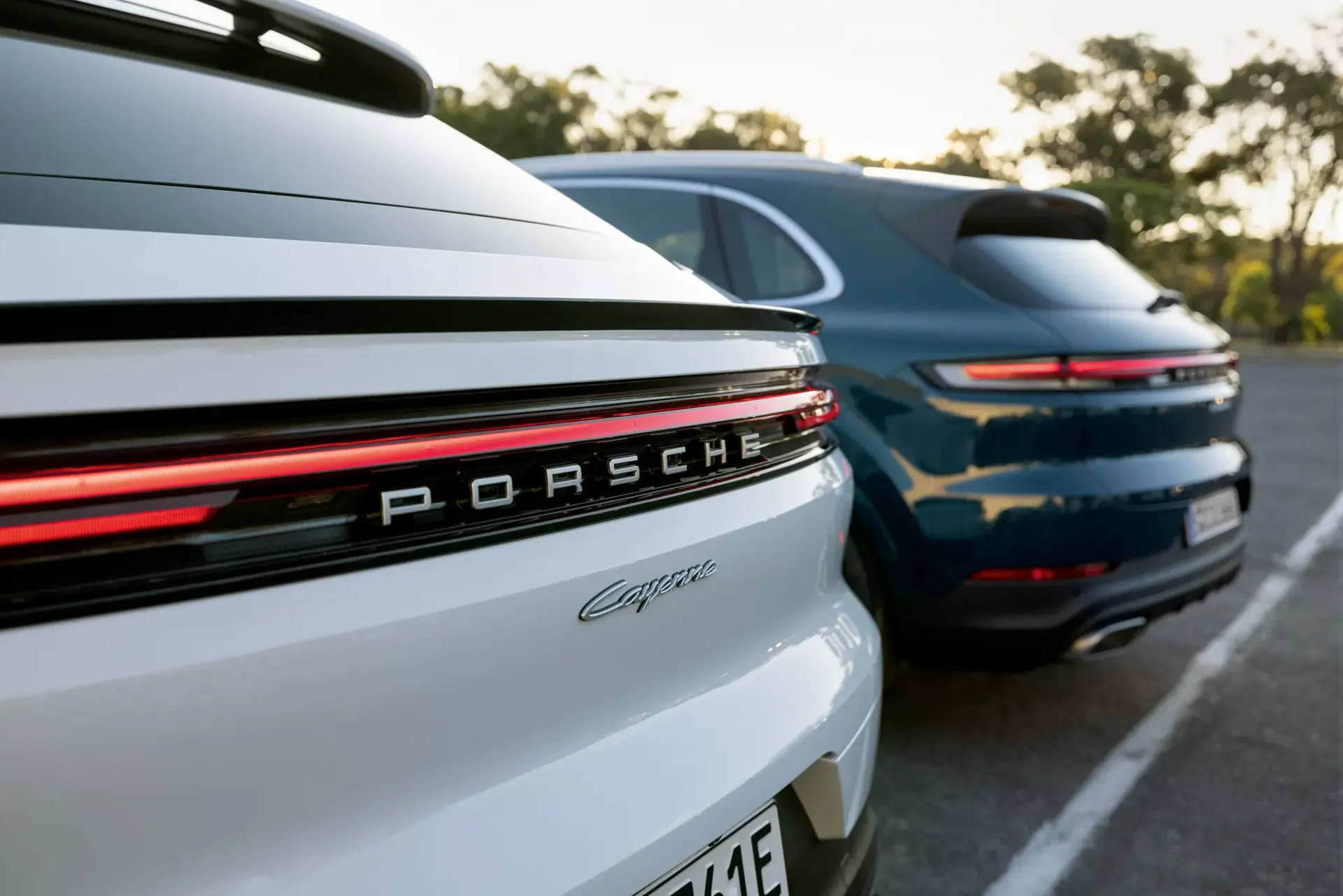 To Porsche Cayenne SUV’er set bagfra på en parkeringsplads i aftensolen.