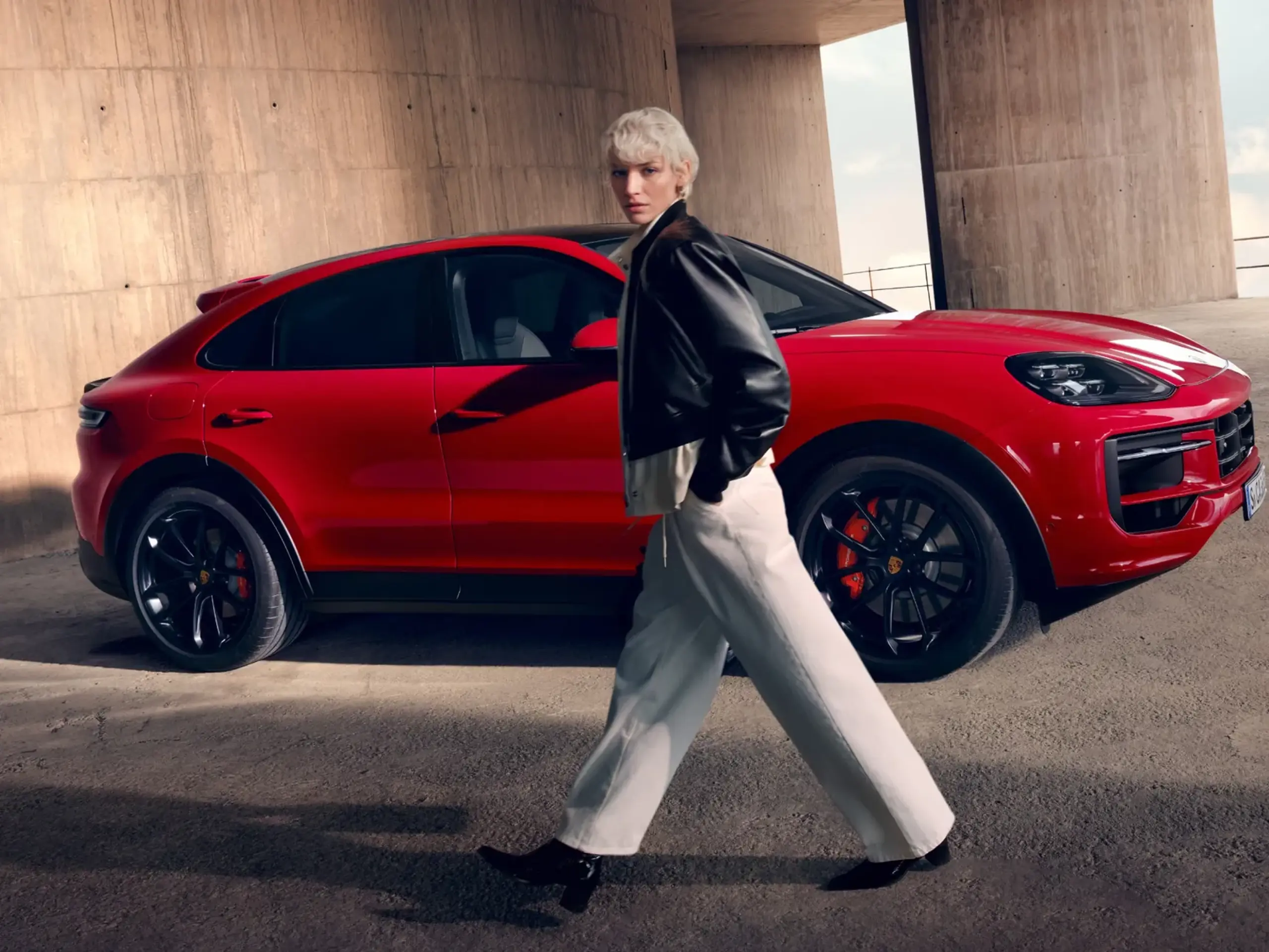 Person går forbi en rød Porsche Cayenne GTS Coupé parkeret under en betonoverdækning.