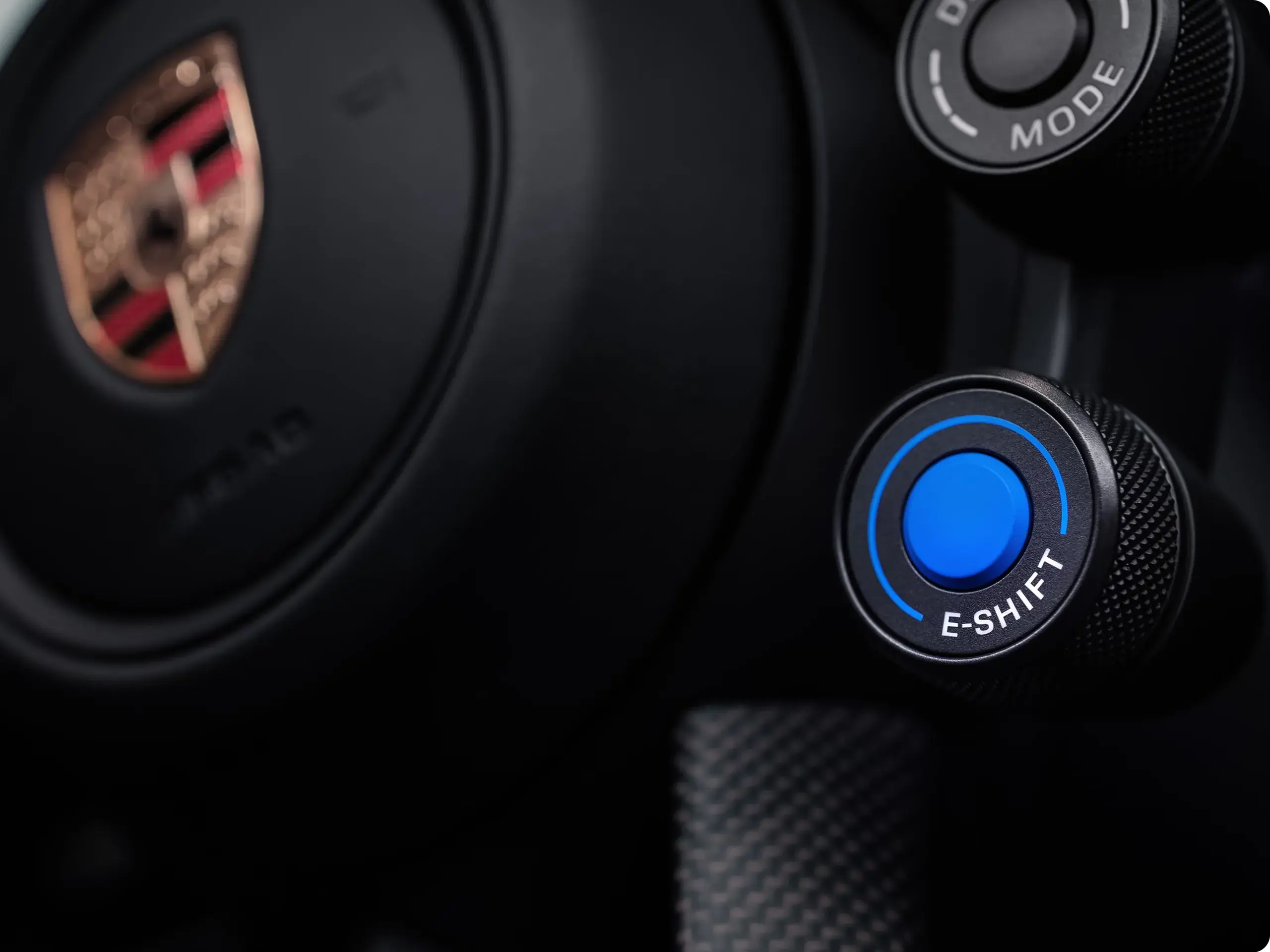 Nærbillede af et Porsche-rat med fokus på en blå knap mærket "E-SHIFT" og en drejeknap med kørselsindstillinger.