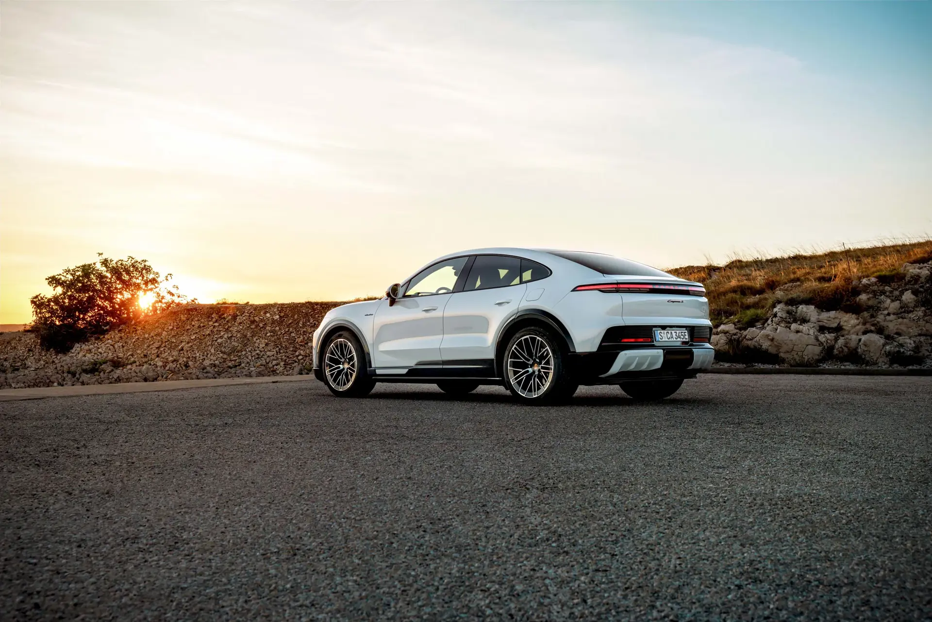 Hvid sportslig coupé-SUV parkeret på en åben vej ved solnedgang i et bakket landskab.