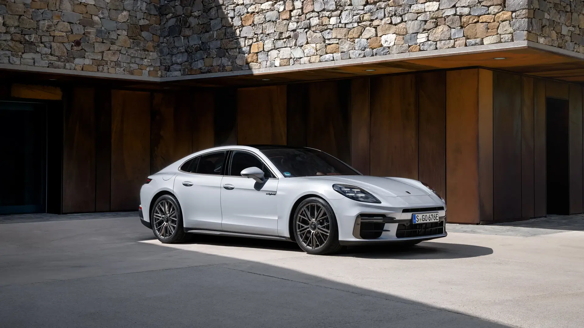 En sølvgrå Porsche Panamera holder parkeret foran en moderne bygning med sten- og metalfacade.