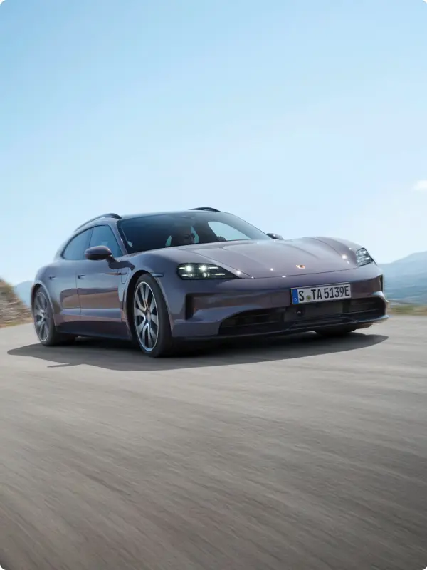 En grå Porsche Taycan 4S Sport Turismo kører hurtigt på en åben vej under blå himmel.