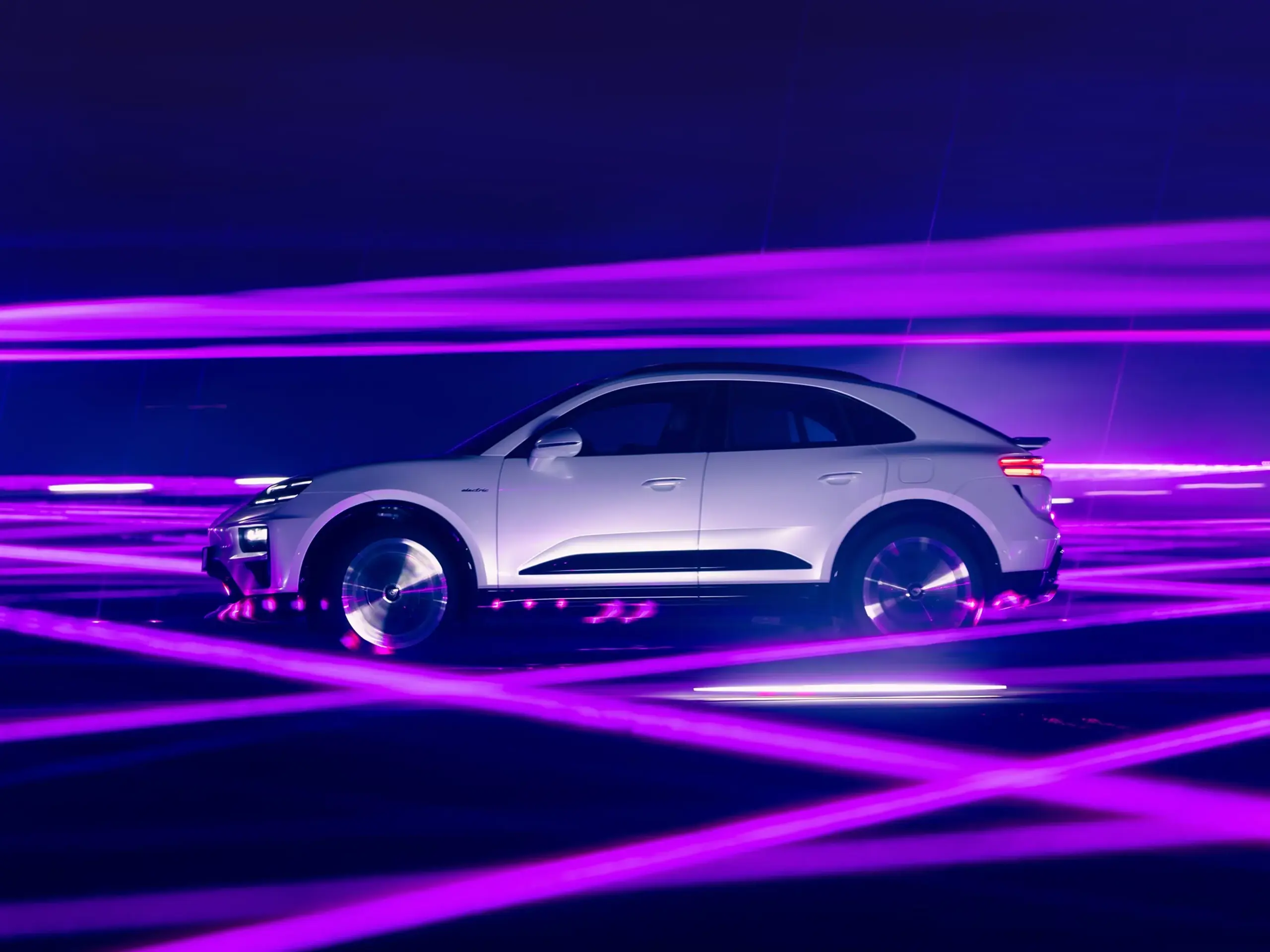 Hvid Porsche Macan Turbo fotograferet fra siden omgivet af dynamiske lilla lysstriber i et mørkt studie.