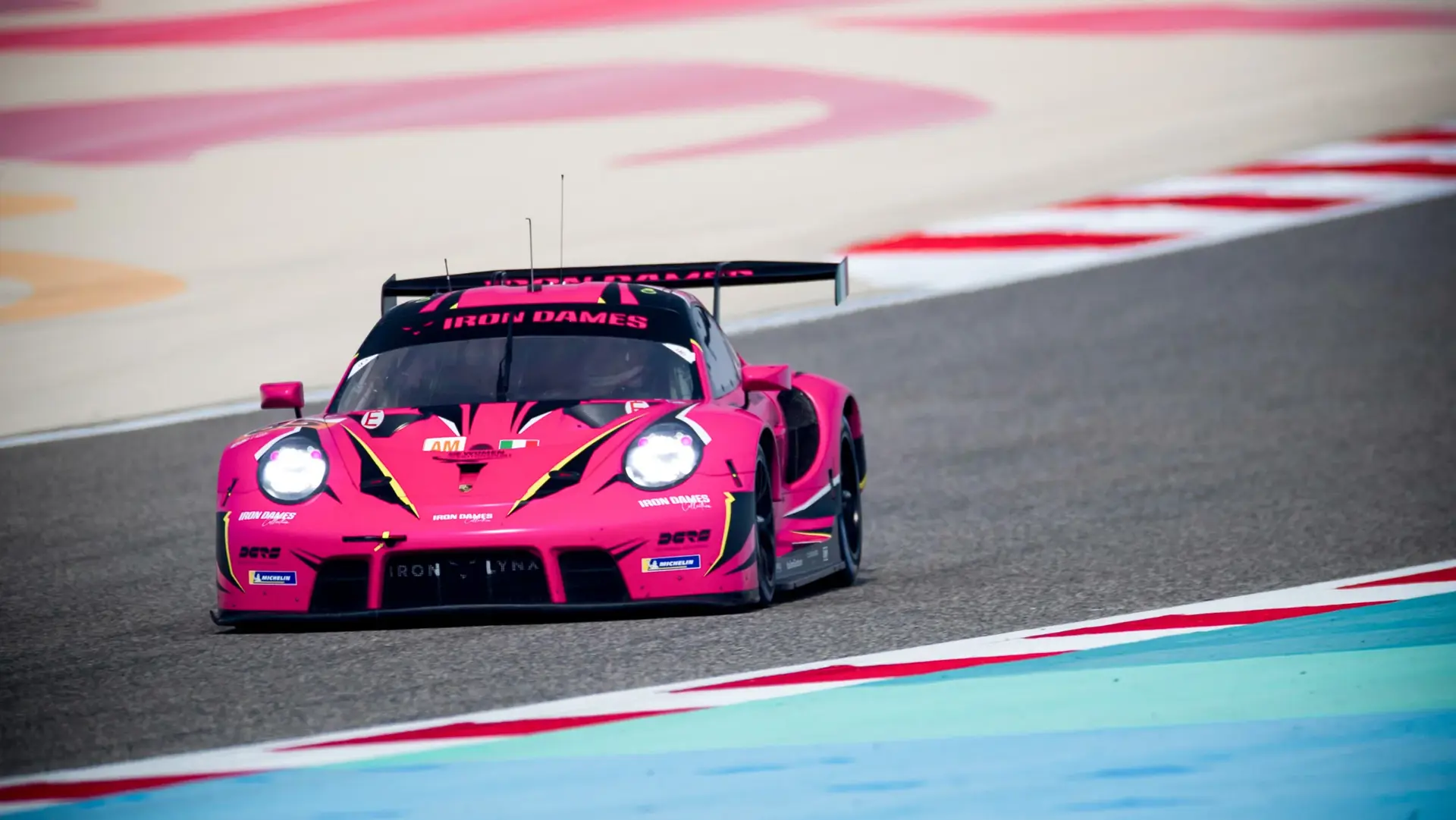 En lyserød racerbils Porsche GT3 med teksten "Iron Dames" kører i høj fart på en racerbane.