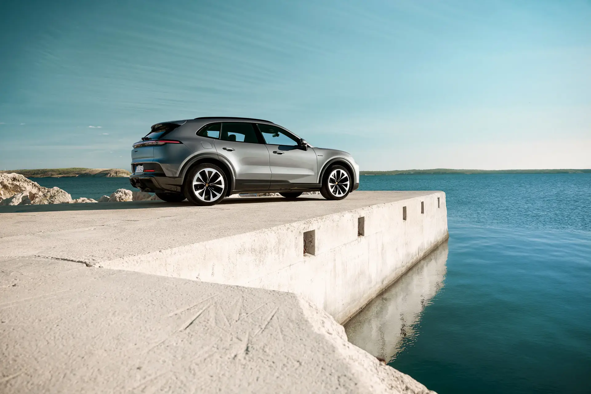 En sølvfarvet SUV holder parkeret yderst på en betonmole ved havet under en klar blå himmel.