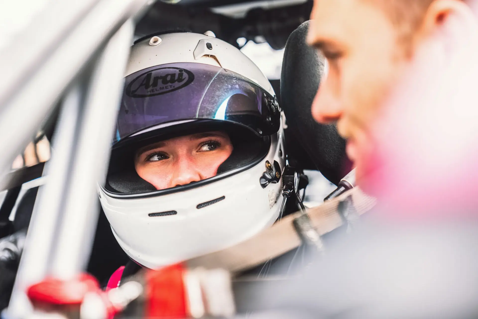 Fører iført hvidt racerhjelm sidder spændt fast i en racerbil, set i nærbillede fra siden.