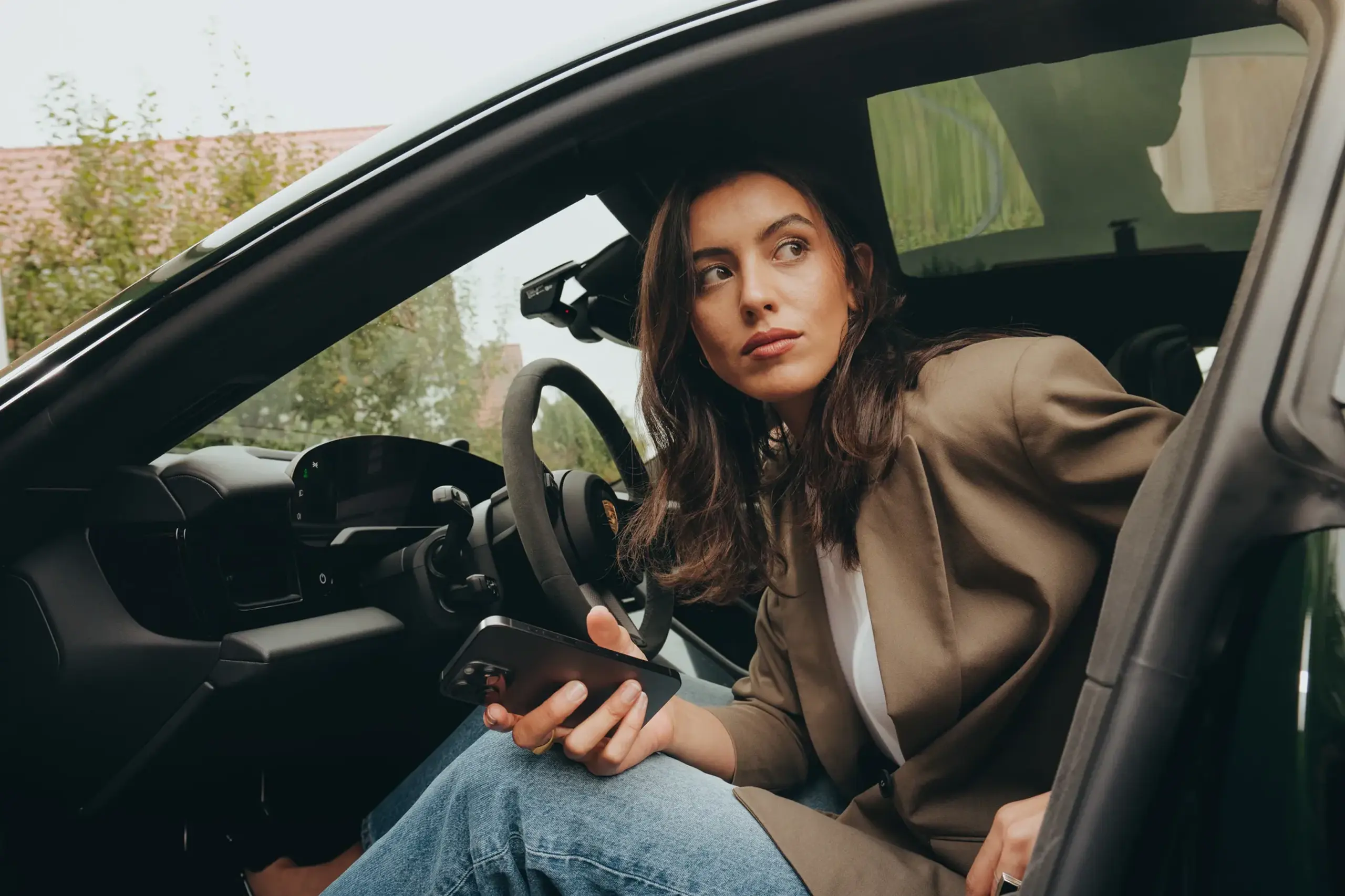 Kvinde sidder i en Porsche og kigger koncentreret på sin smartphone, mens hun bruger en app.