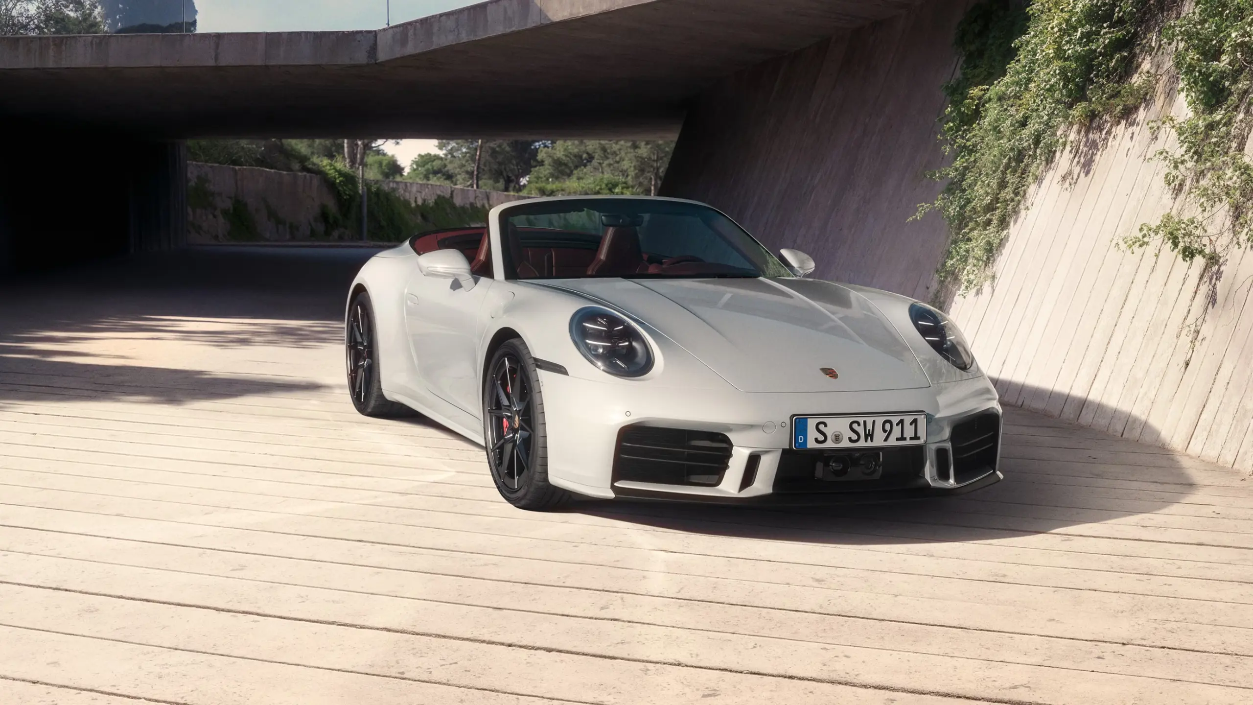 Hvid Porsche 911 Cabriolet med rød kabine holder parkeret på en lys, moderne gårdsplads i sollys.