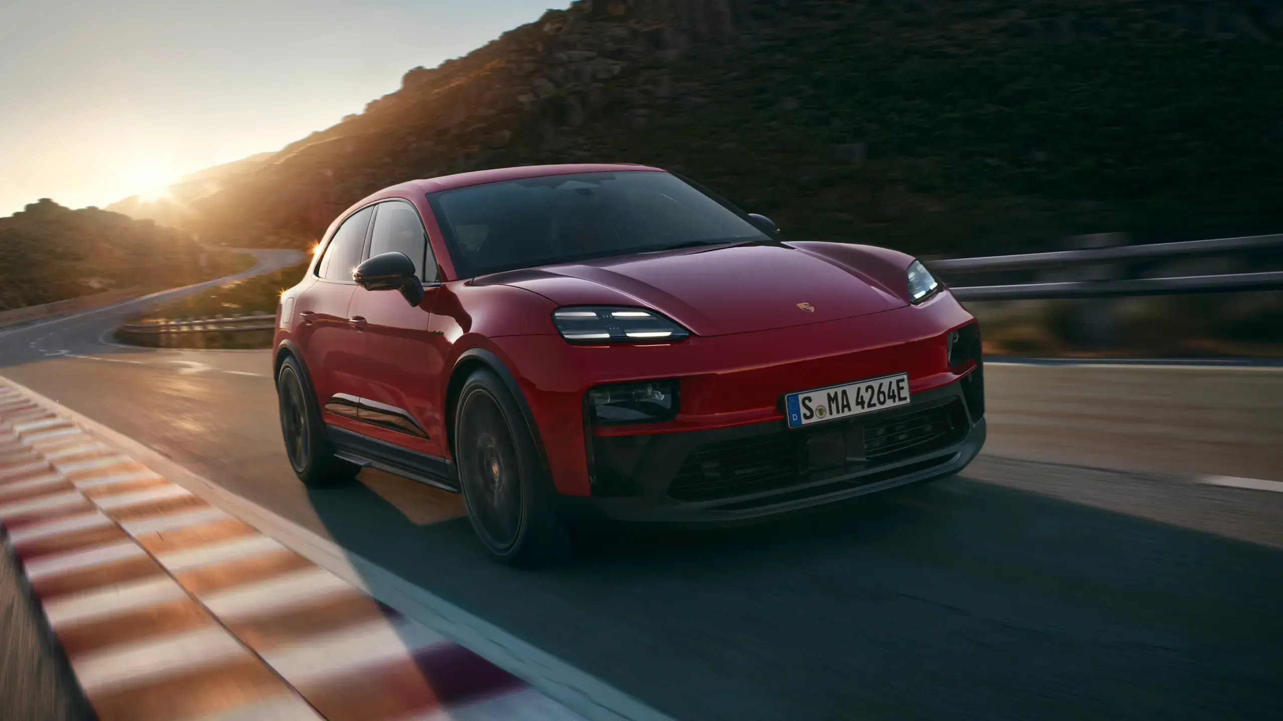 Rød Porsche Macan GTS set bagfra parkeret på en landevej med dramatiske skyer i baggrunden.