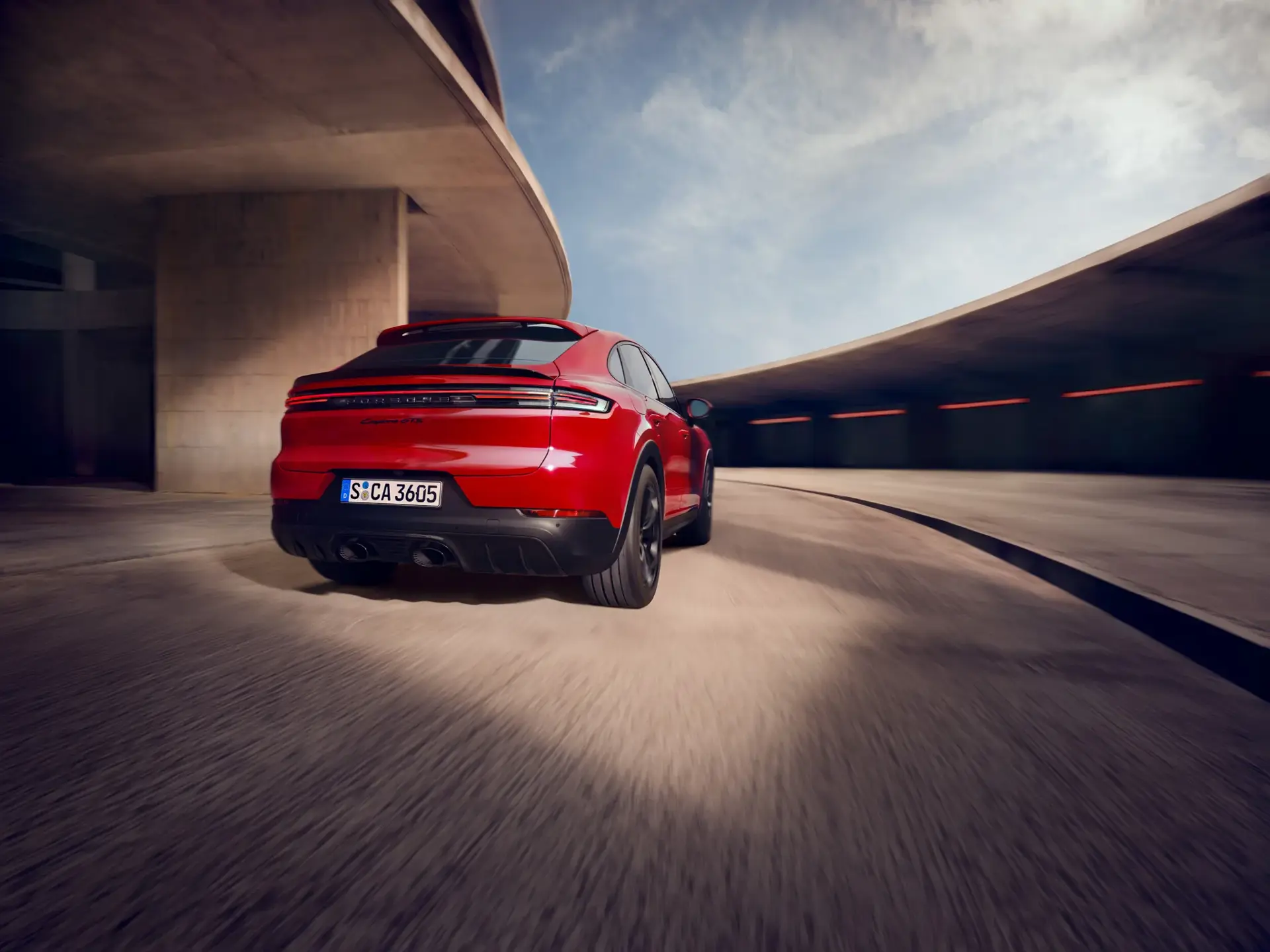 Rød Porsche Cayenne GTS Coupé set bagfra i fart på en kurvet, moderne betonvej.