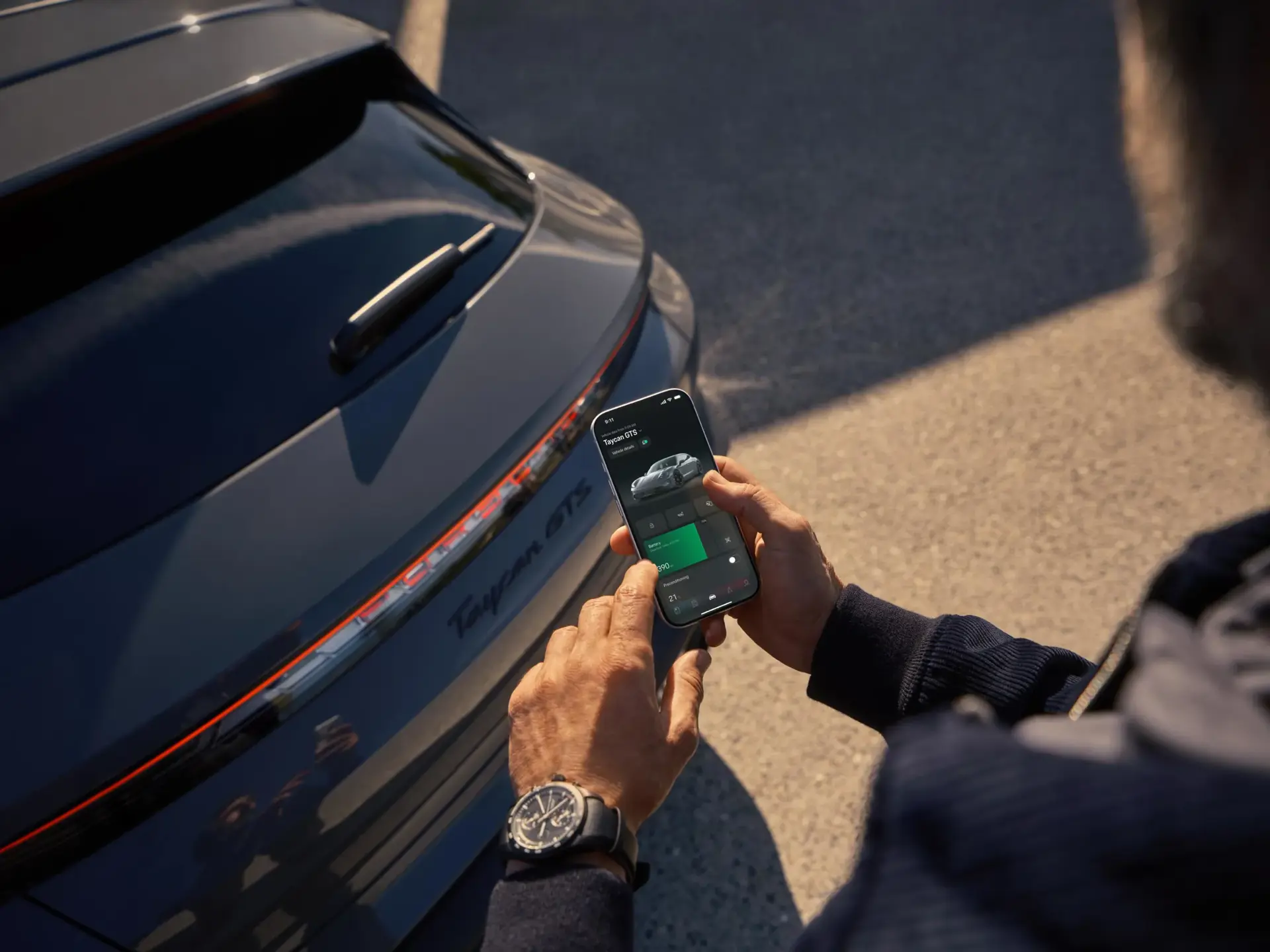 Person styrer en Porsche Taycan via en app på sin smartphone ved bilens bagende.