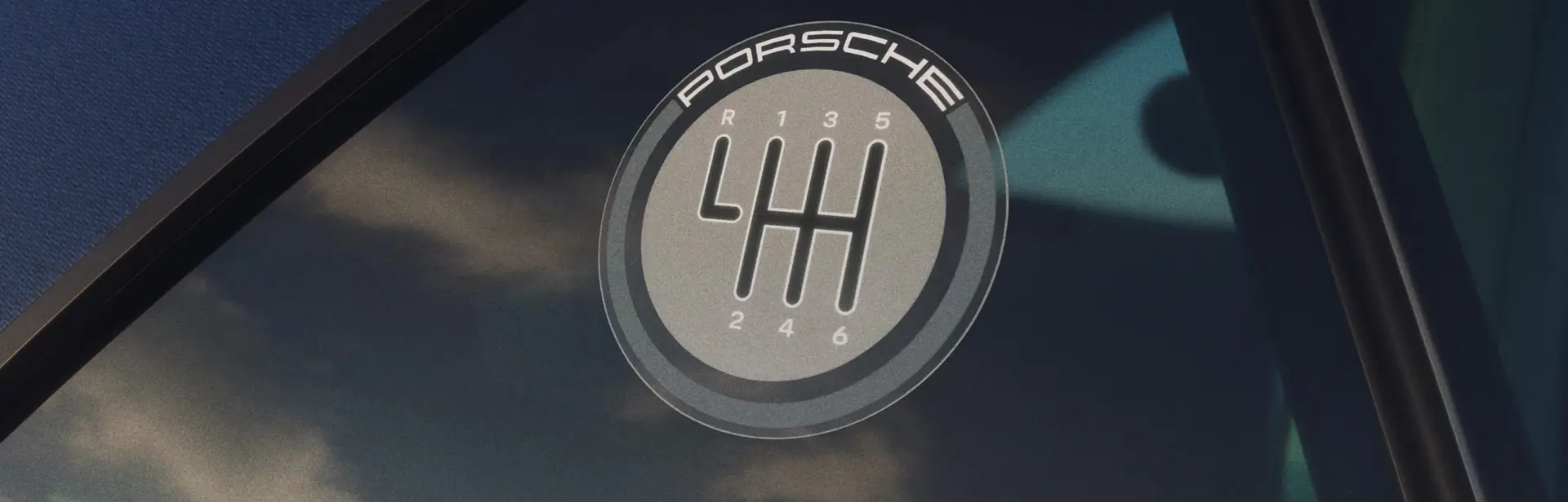 Nærbillede af et Porsche-logo med et manuelt gearskema på en rude i en 911 Carrera T Cabriolet.