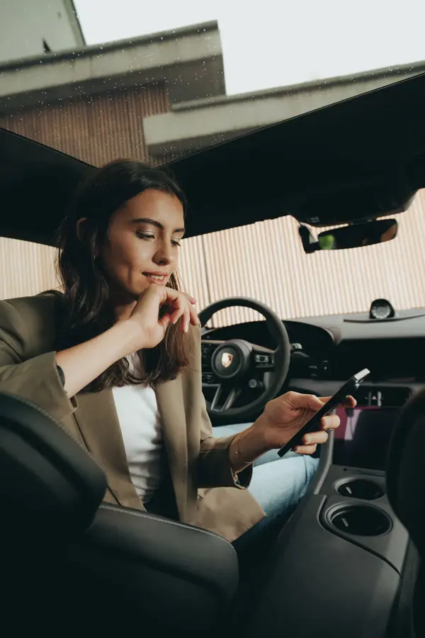 Kvinde sidder i en Porsche og kigger koncentreret på sin smartphone, mens hun bruger en app.
