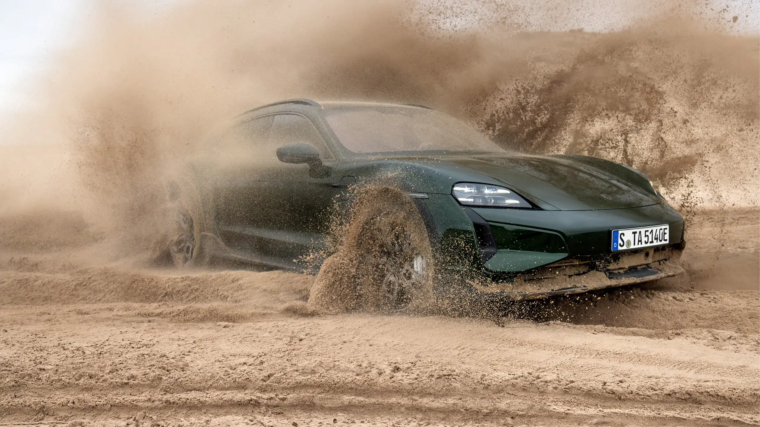 En mørkegrøn Porsche Taycan Turbo Cross Turismo ses bagfra, mens den kører hurtigt gennem et sandet ørkenlandskab.