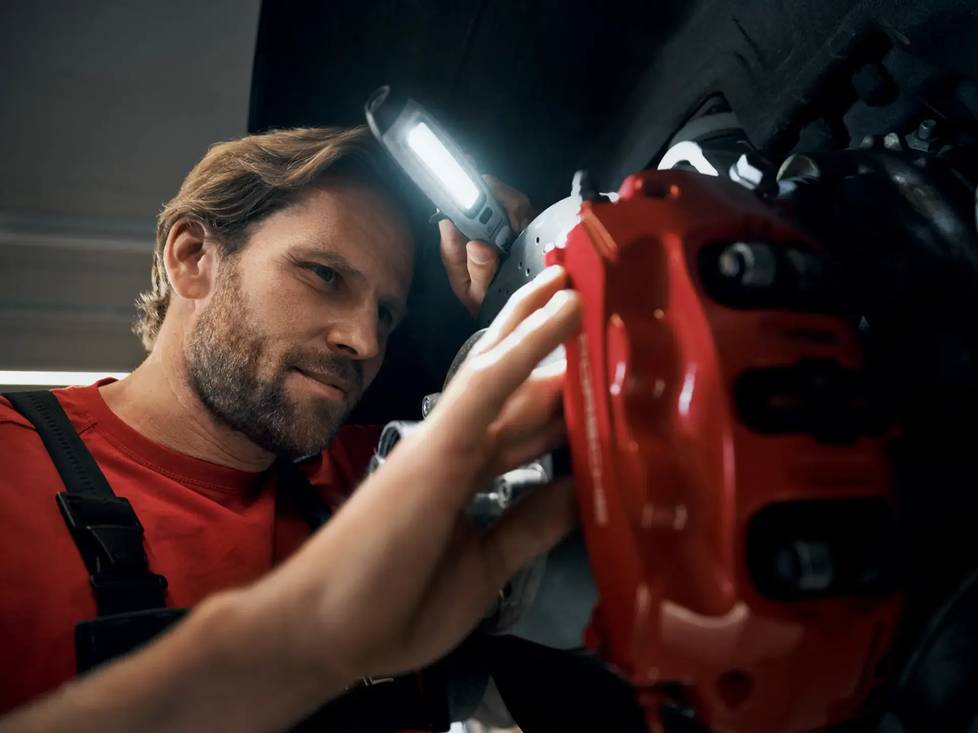Mekaniker inspicerer en Porsche-bremsekaliber med en håndlampe.