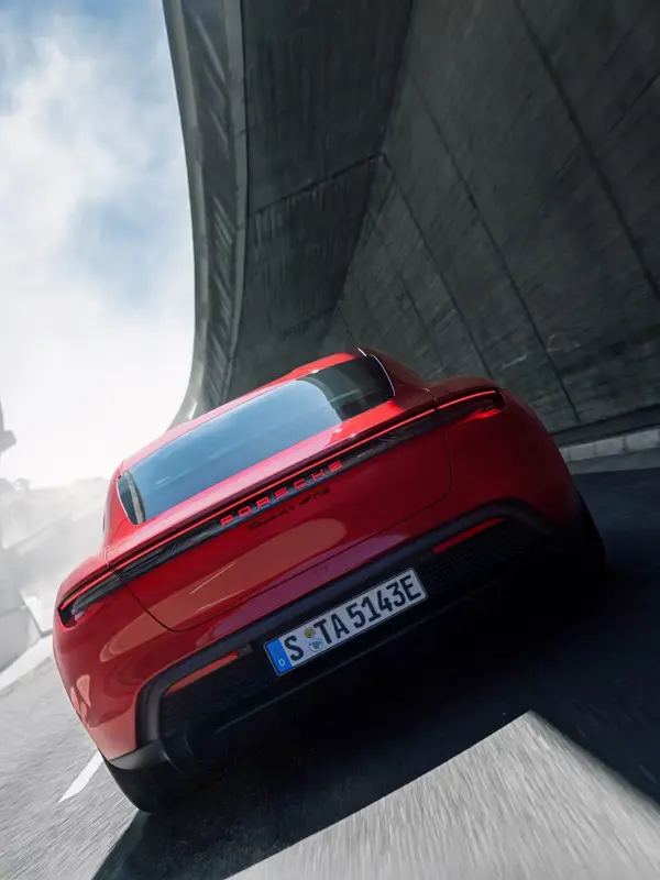 En rød Porsche Taycan ses bagfra, mens den kører gennem en kurvet bytunnel i høj fart.