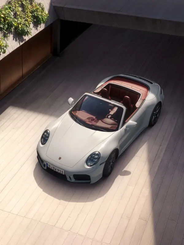 Hvid Porsche 911 Cabriolet med rød kabine holder parkeret på en lys, moderne gårdsplads i sollys.