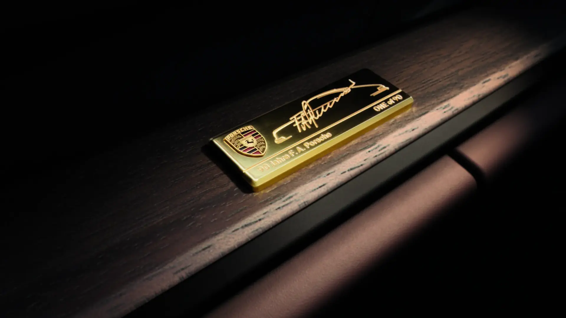 Guldplakette med Porsche-logo og indgravering monteret på en mørk træpanel i bilens interiør.