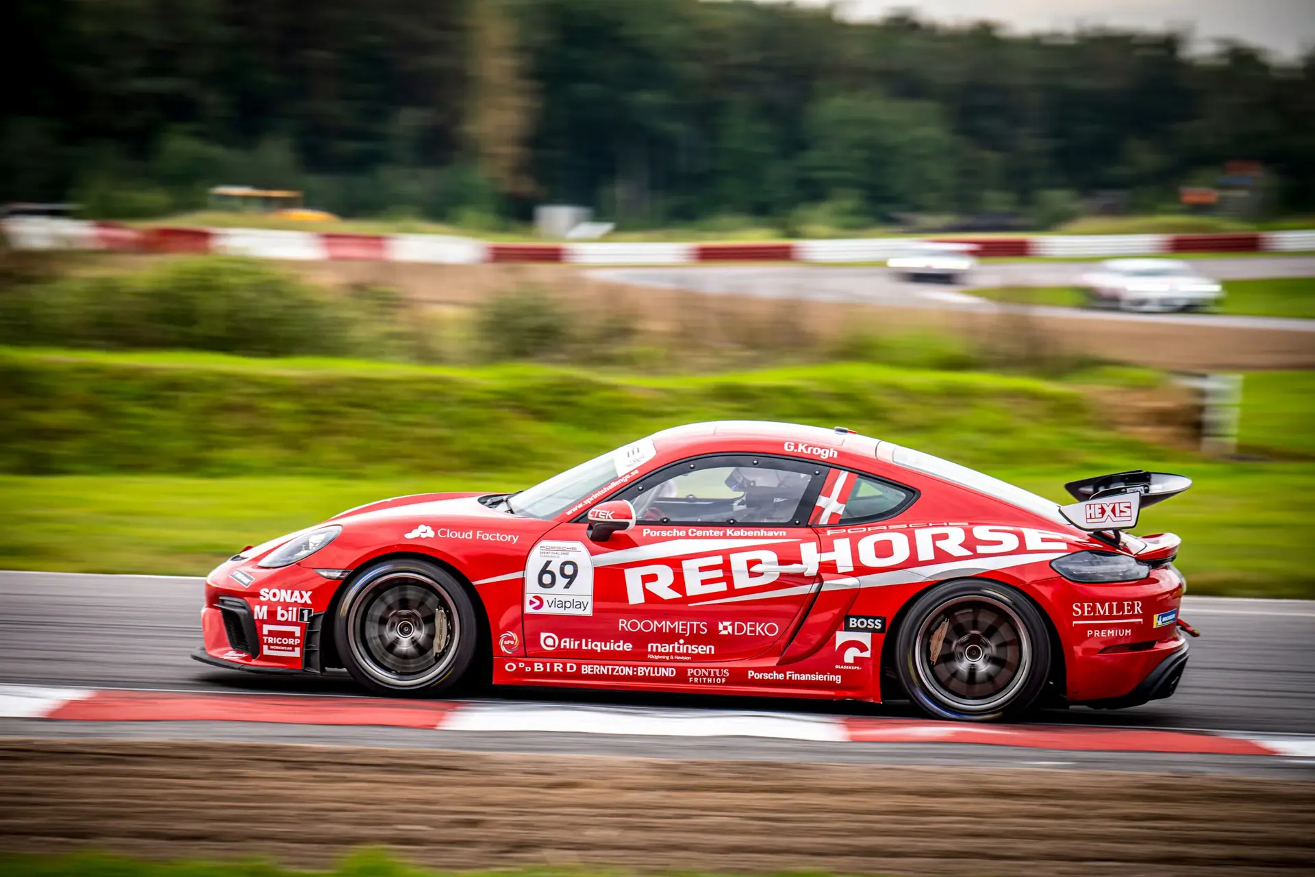 Rød Porsche-racerbil med startnummer 69 kører i høj fart på racerbane ved Mantorp.