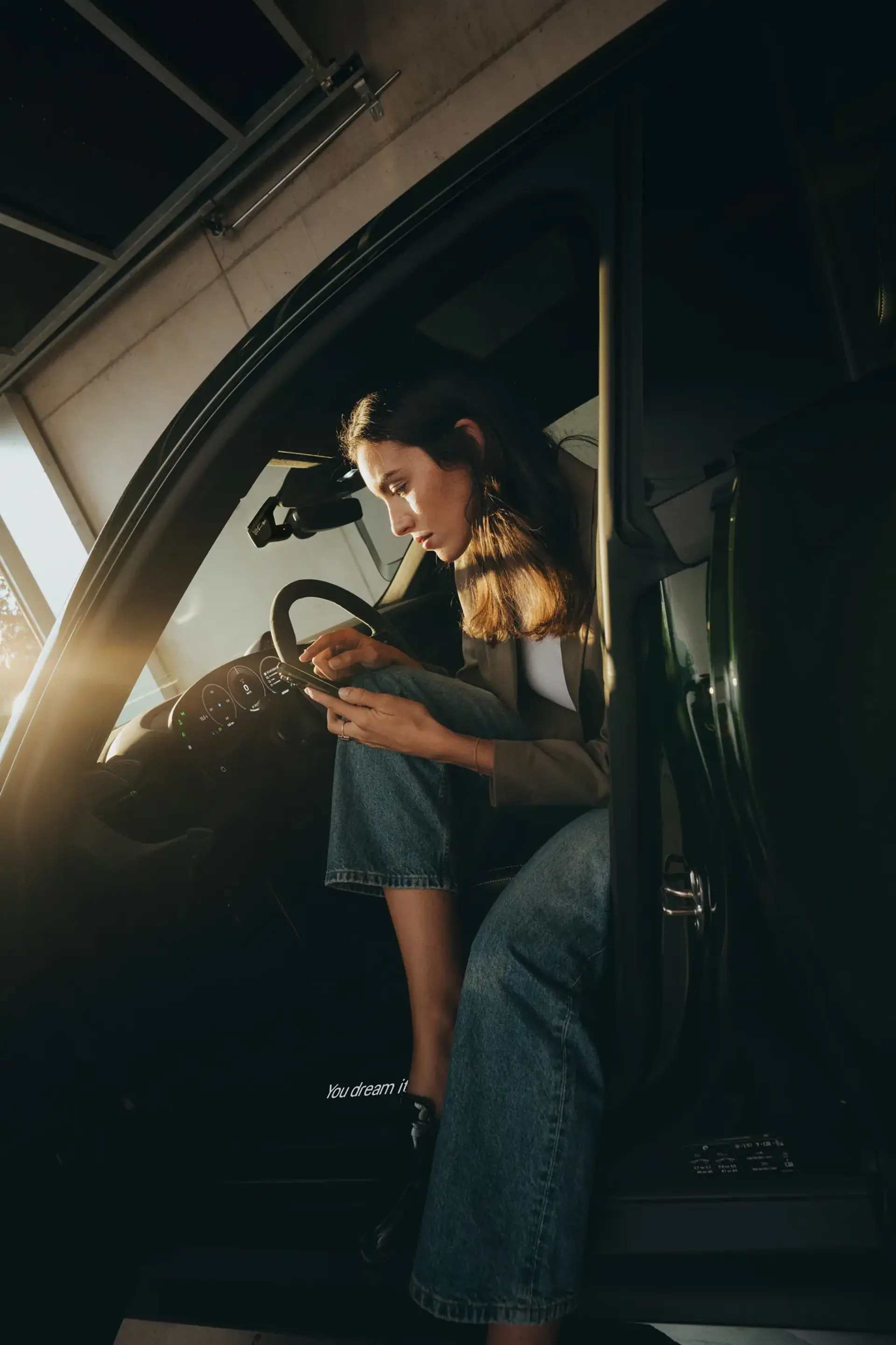 Kvinde sidder i en bil og bruger sin smartphone, mens døren står åben i en garage.