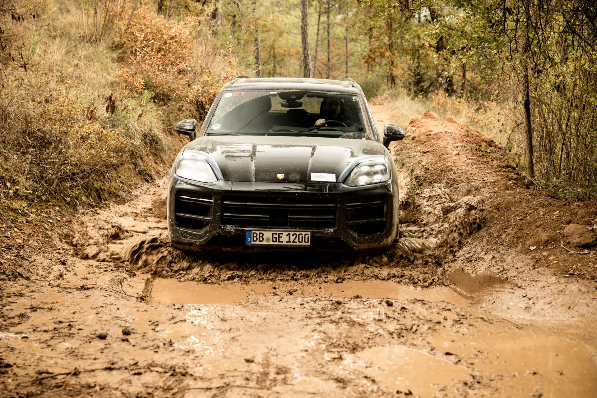 Sort SUV, der kører gennem en mudret skovvej med vandpytter.