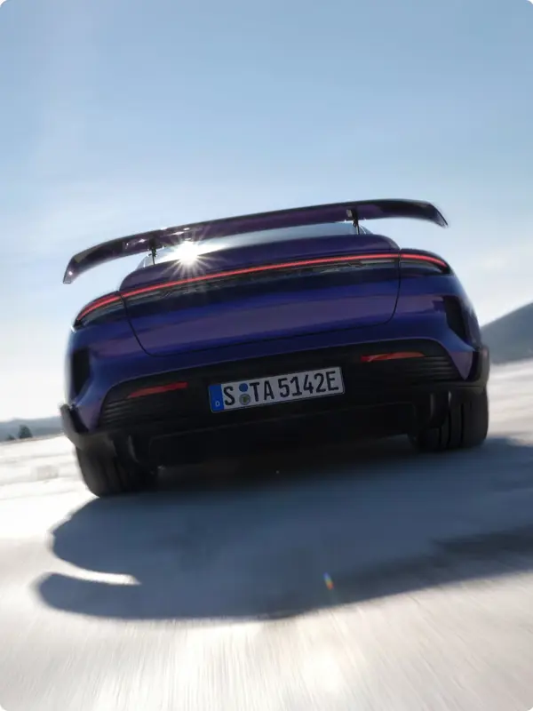 Bagfra-vinkel af en blå Porsche Taycan Turbo GT med stor hækspoiler i fart på en solrig vej.